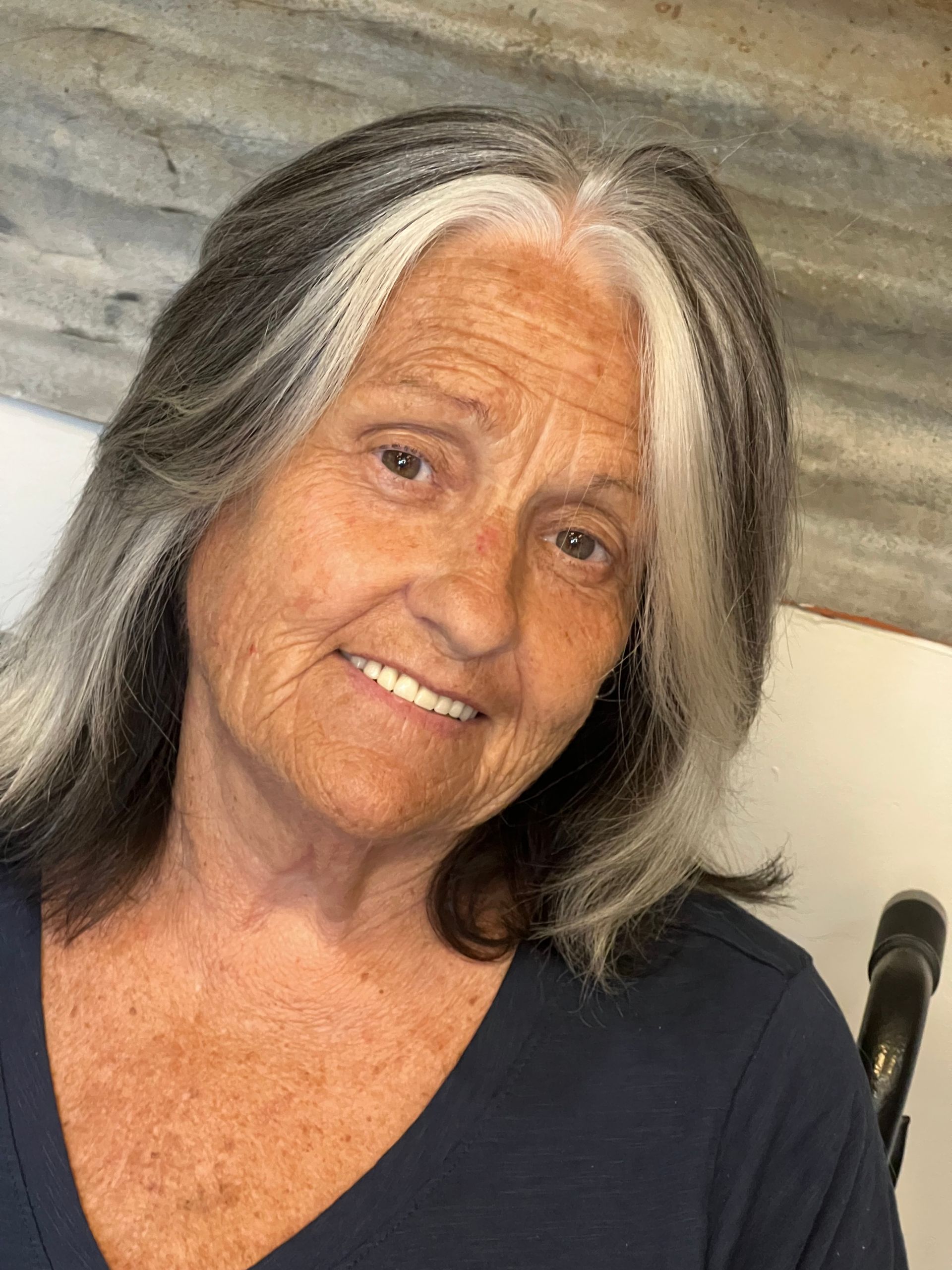 A woman with gray hair and white streaks is smiling for the camera.