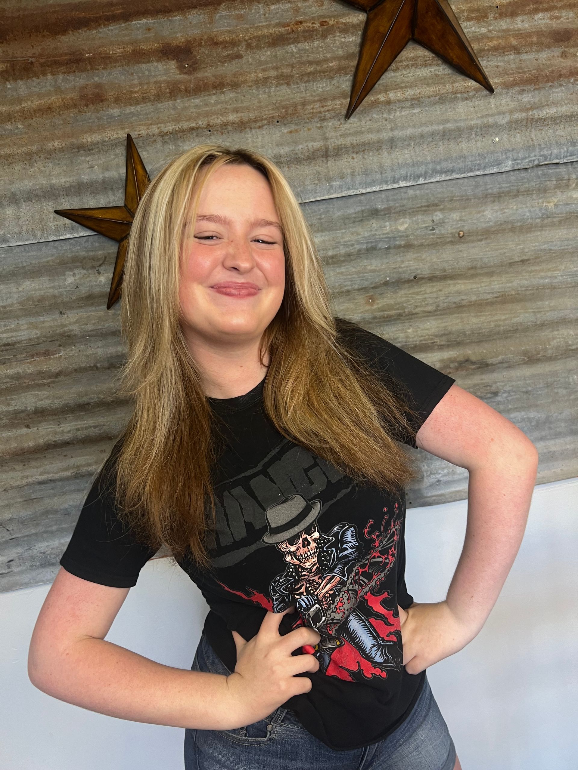 A young girl wearing a black t-shirt and shorts is standing with her hands on her hips and smiling.