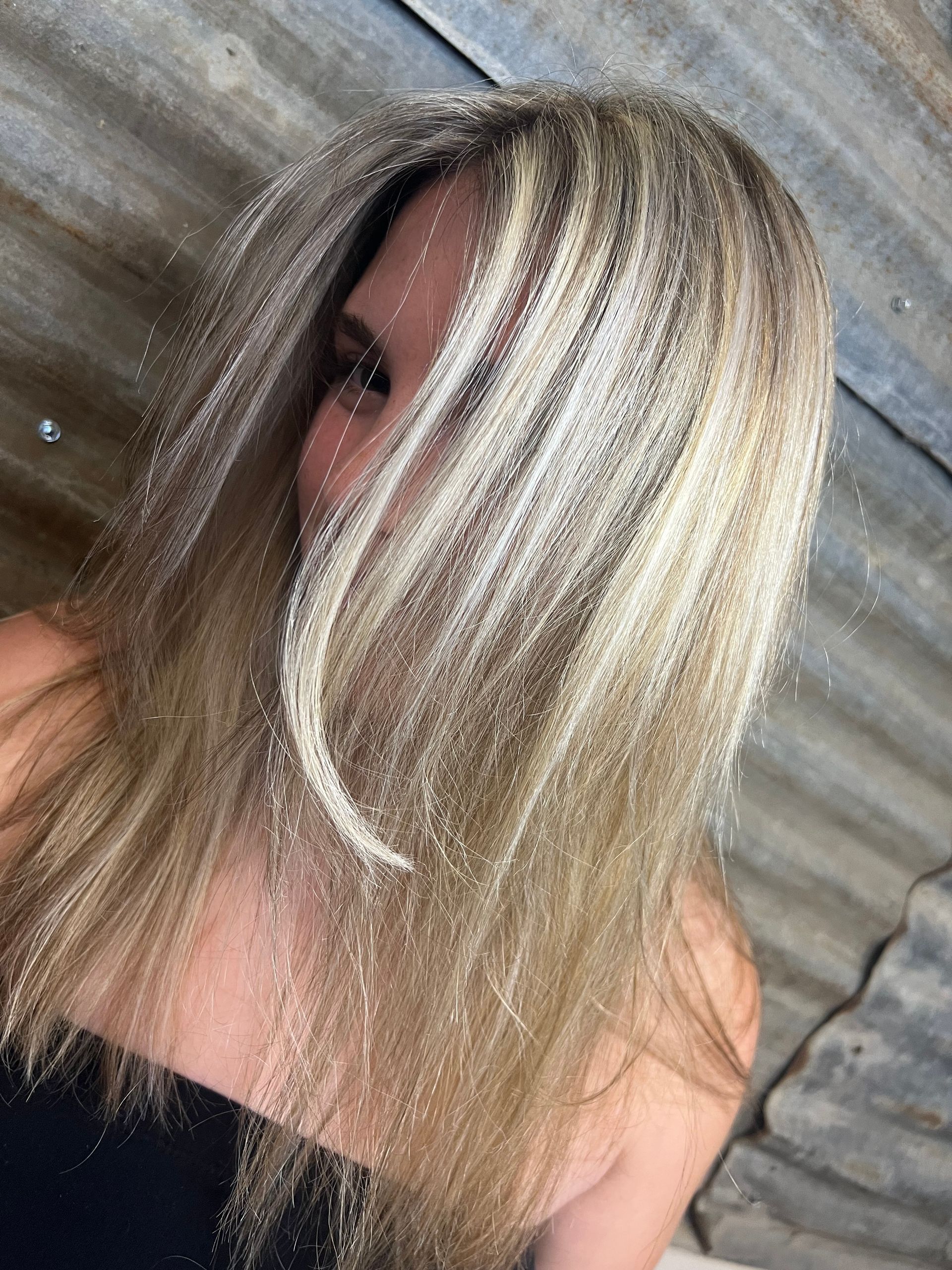 A woman with long blonde hair is covering her face with her hair.