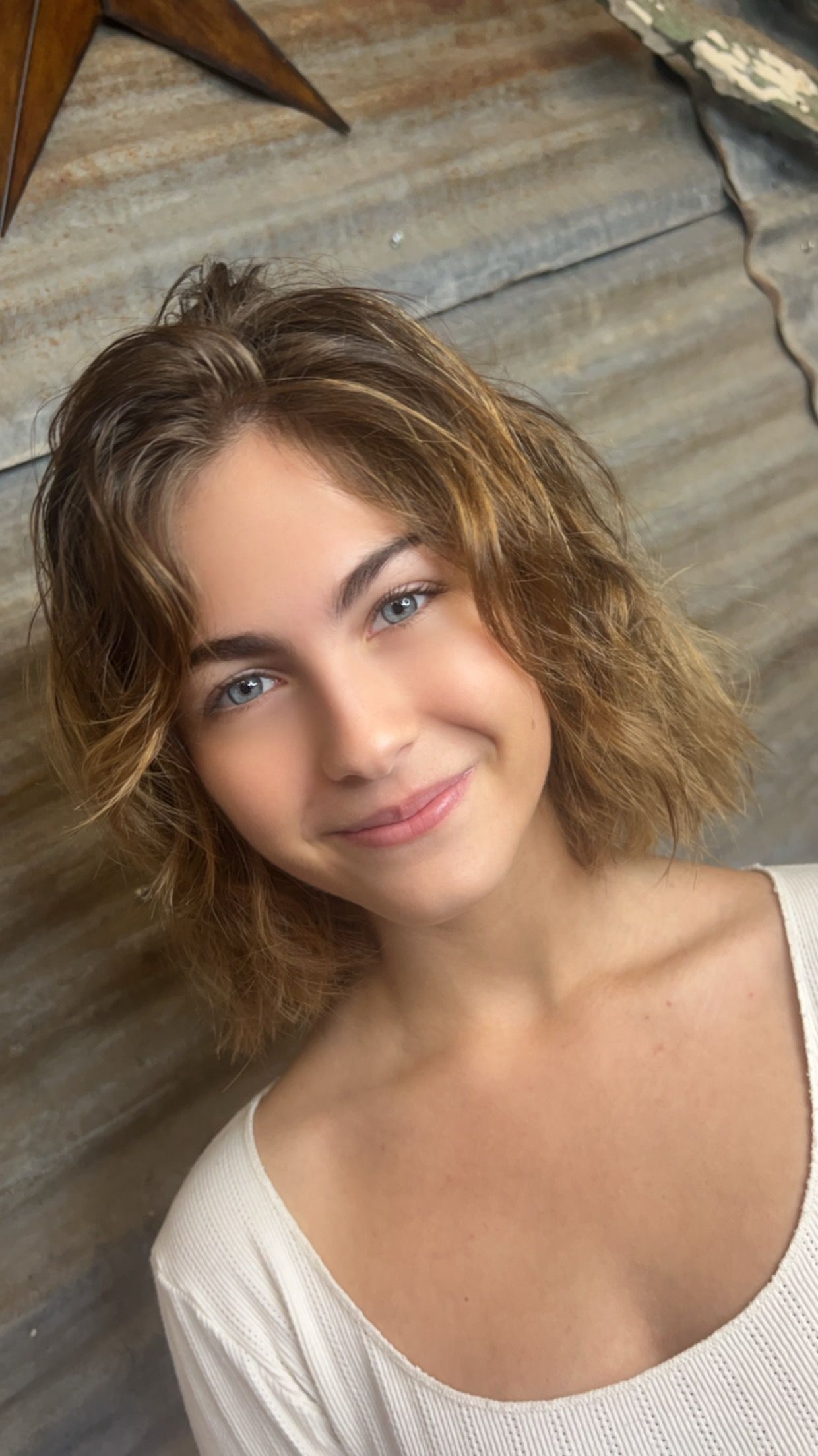 A young woman with short hair is smiling and wearing a white shirt.