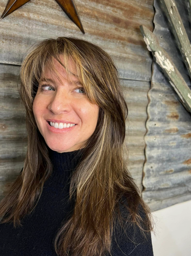 A woman with long brown hair and a black turtleneck is smiling.