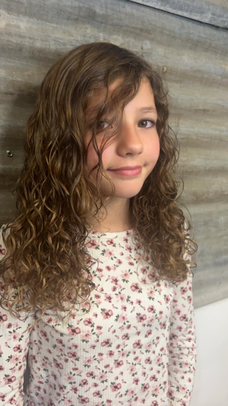 A young girl with curly hair is wearing a floral shirt.