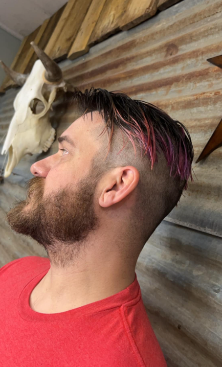 A man with a beard and pink hair is standing in front of a skull.