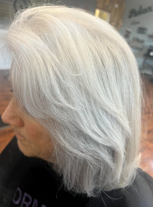 A woman with gray hair is sitting in a chair in a salon.