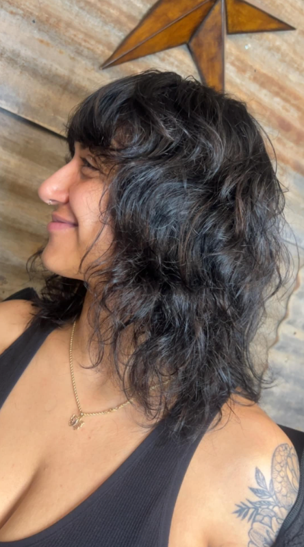 A woman with curly hair is smiling and wearing a black tank top.