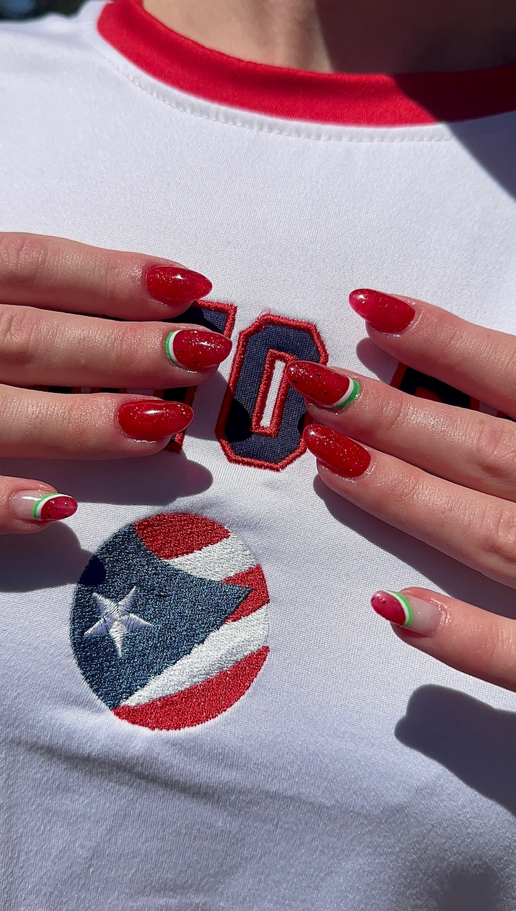 A woman with red nails is wearing a white shirt with a puerto rico flag on it.
