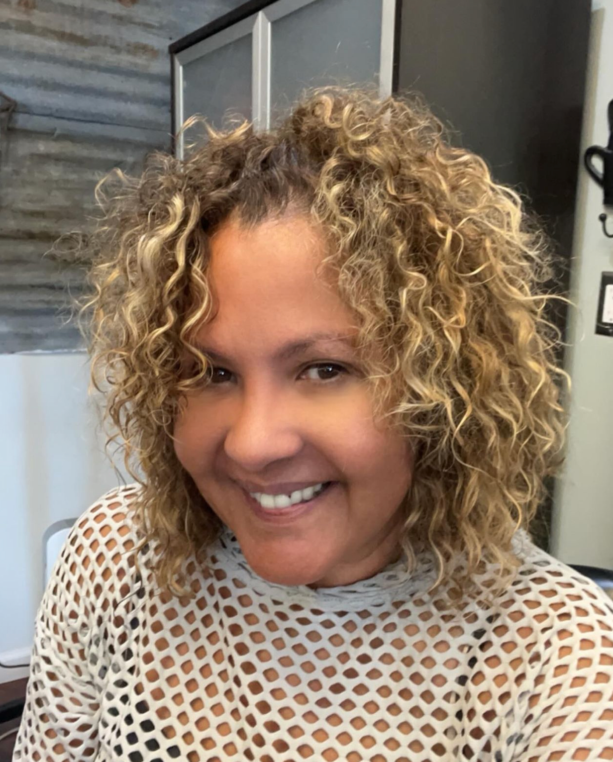 A woman with curly hair is smiling and wearing a white shirt.