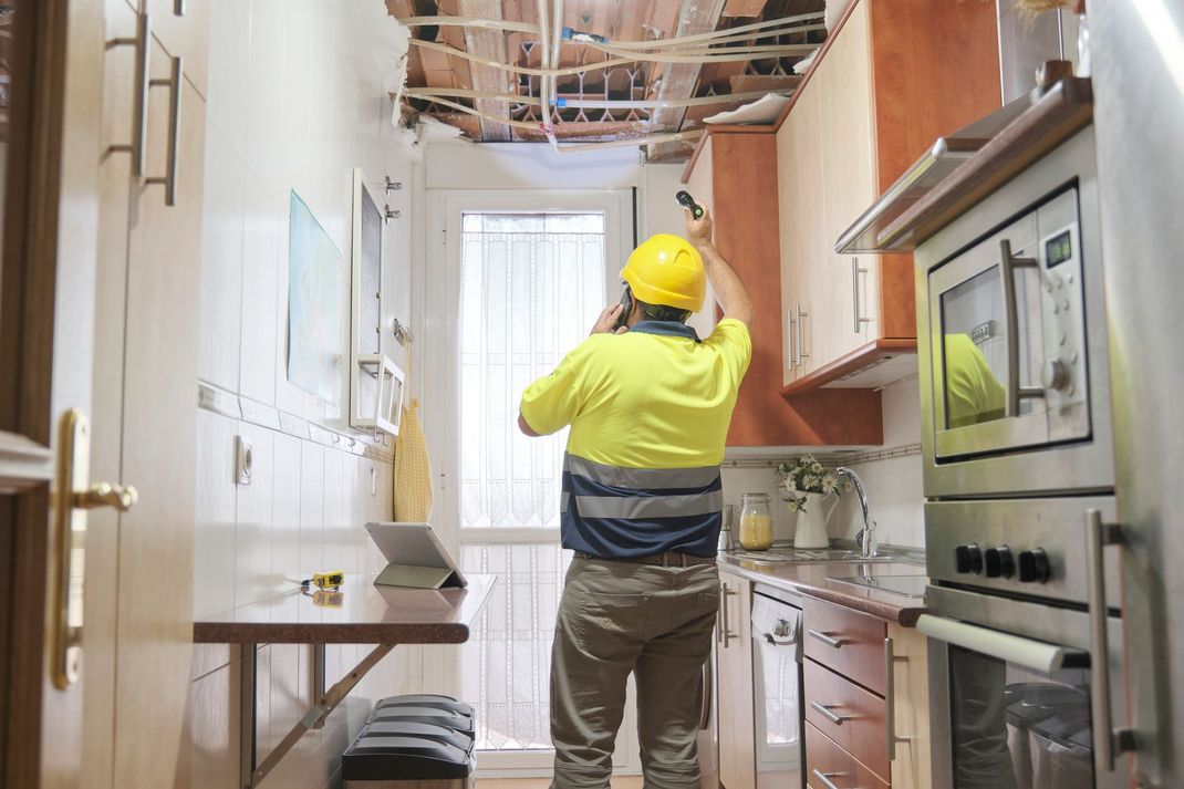 A man in a hard hat is standing in a kitchen looking at the ceiling.