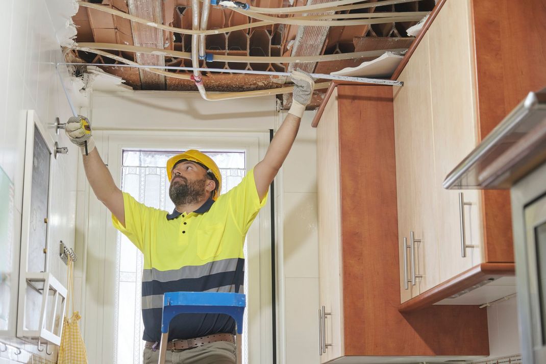 A man is working on the ceiling of a kitchen.