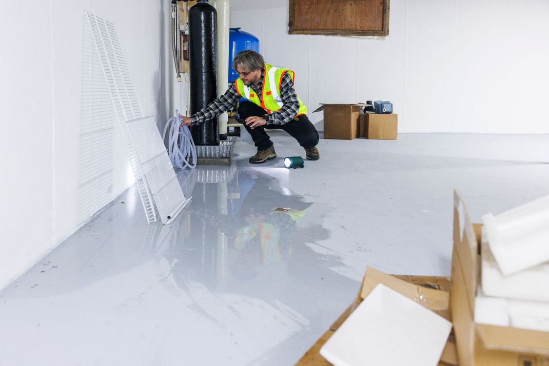 A man in a yellow vest is kneeling on the floor in a room.