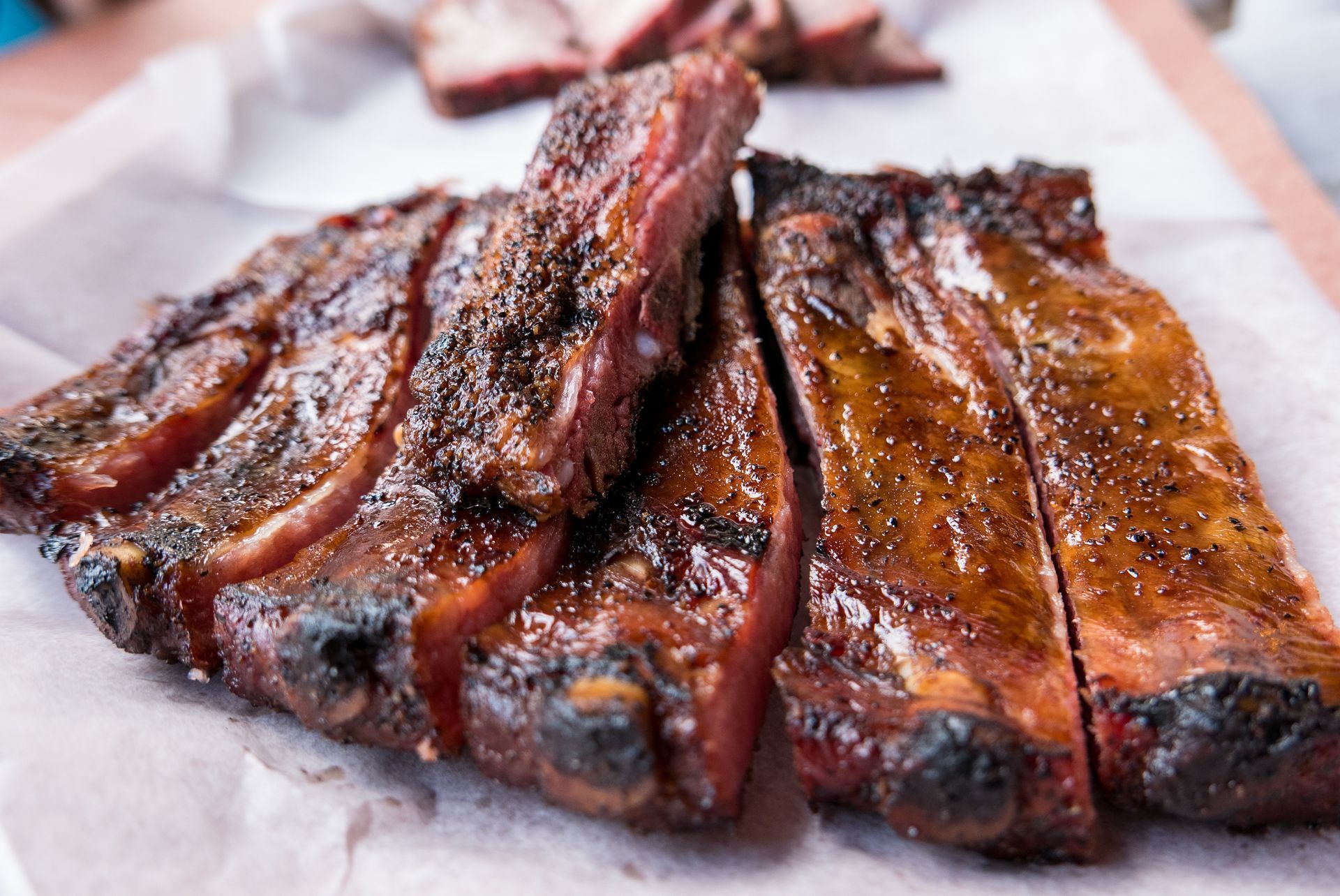 Glazed smoked ribs on parchment paper, sliced into portions with a dark, glossy crust