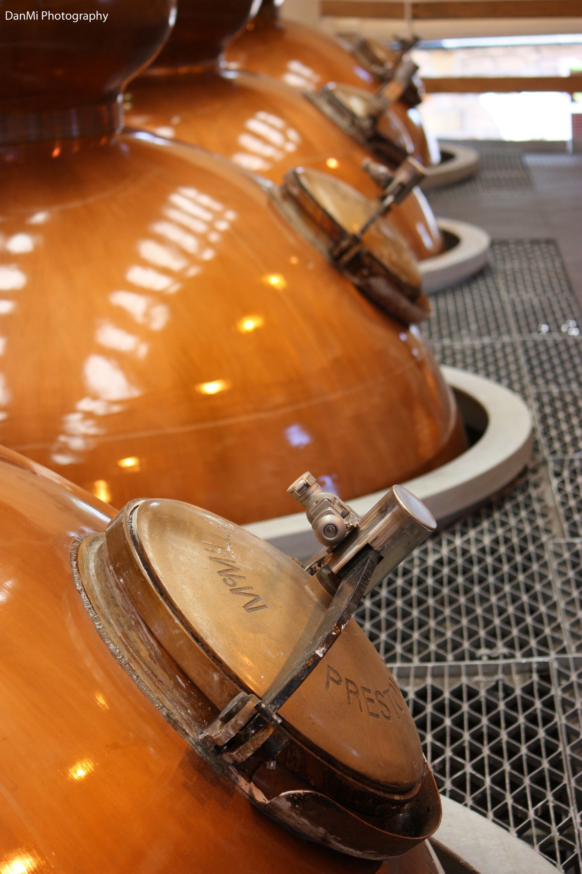 Rows of large orange-brown wooden barrels in a cellar, with metal hoops and grated flooring.
