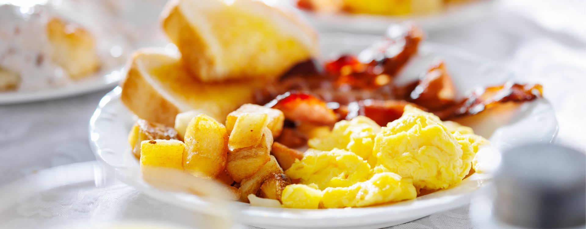 Breakfast plate with scrambled eggs, toast, and bacon on a white table