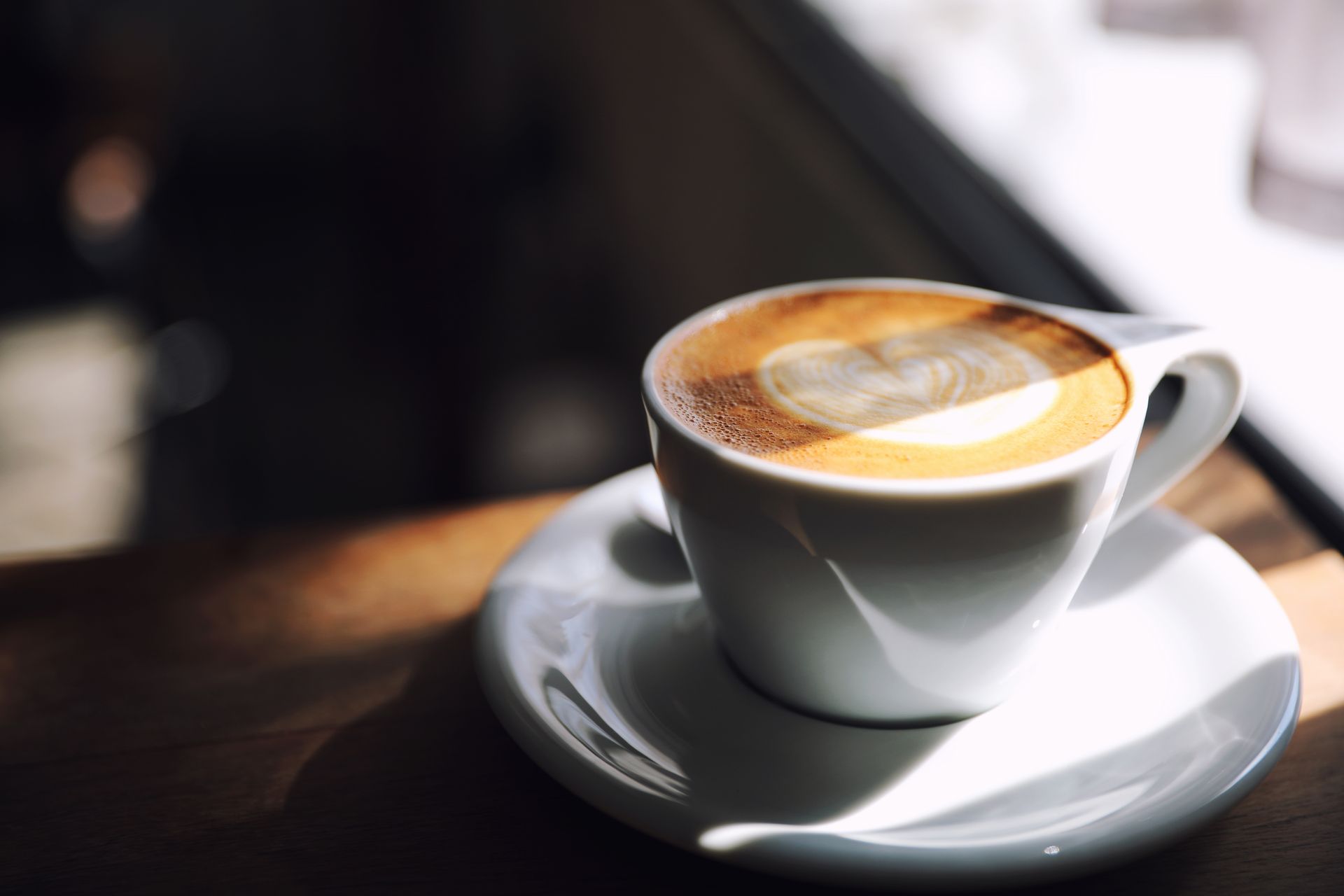 White cup of latte on saucer with heart-shaped foam on a sunlit table