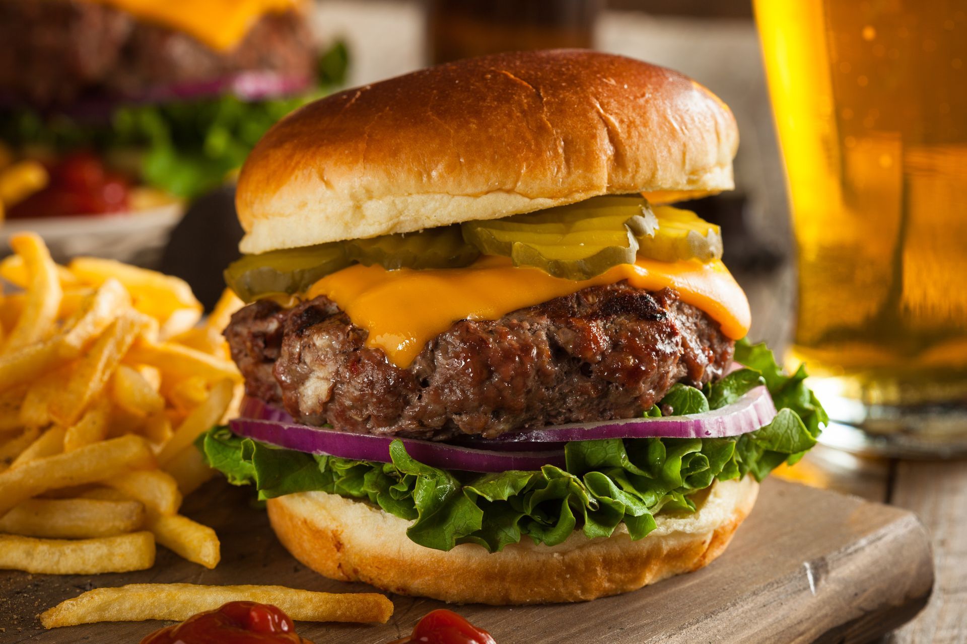 Juicy cheeseburger with lettuce, onion, and fries on a wooden board