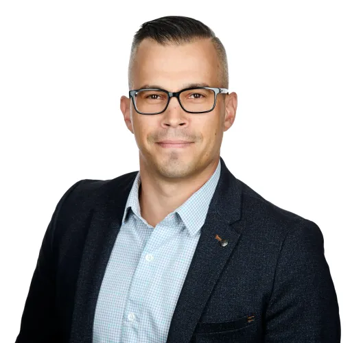 Man with glasses, wearing a blazer over a button-down shirt, looking at the viewer.