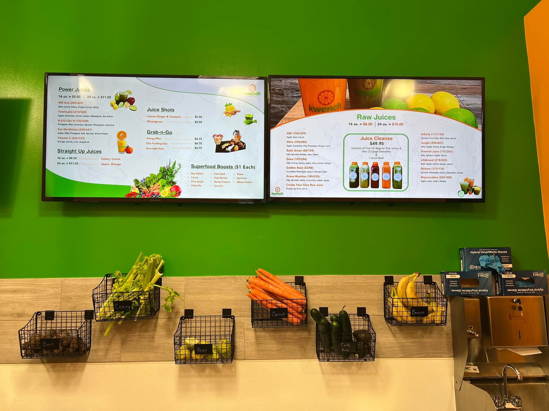 Two menu screens above a counter with produce baskets, green wall.
