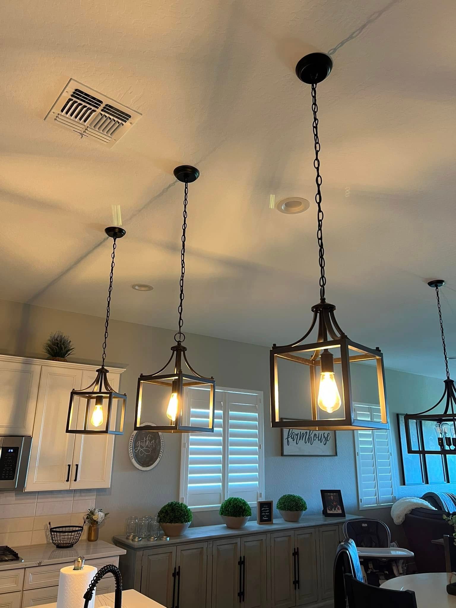 Three pendant lights hanging above a kitchen island, each with a glass and metal lantern design.