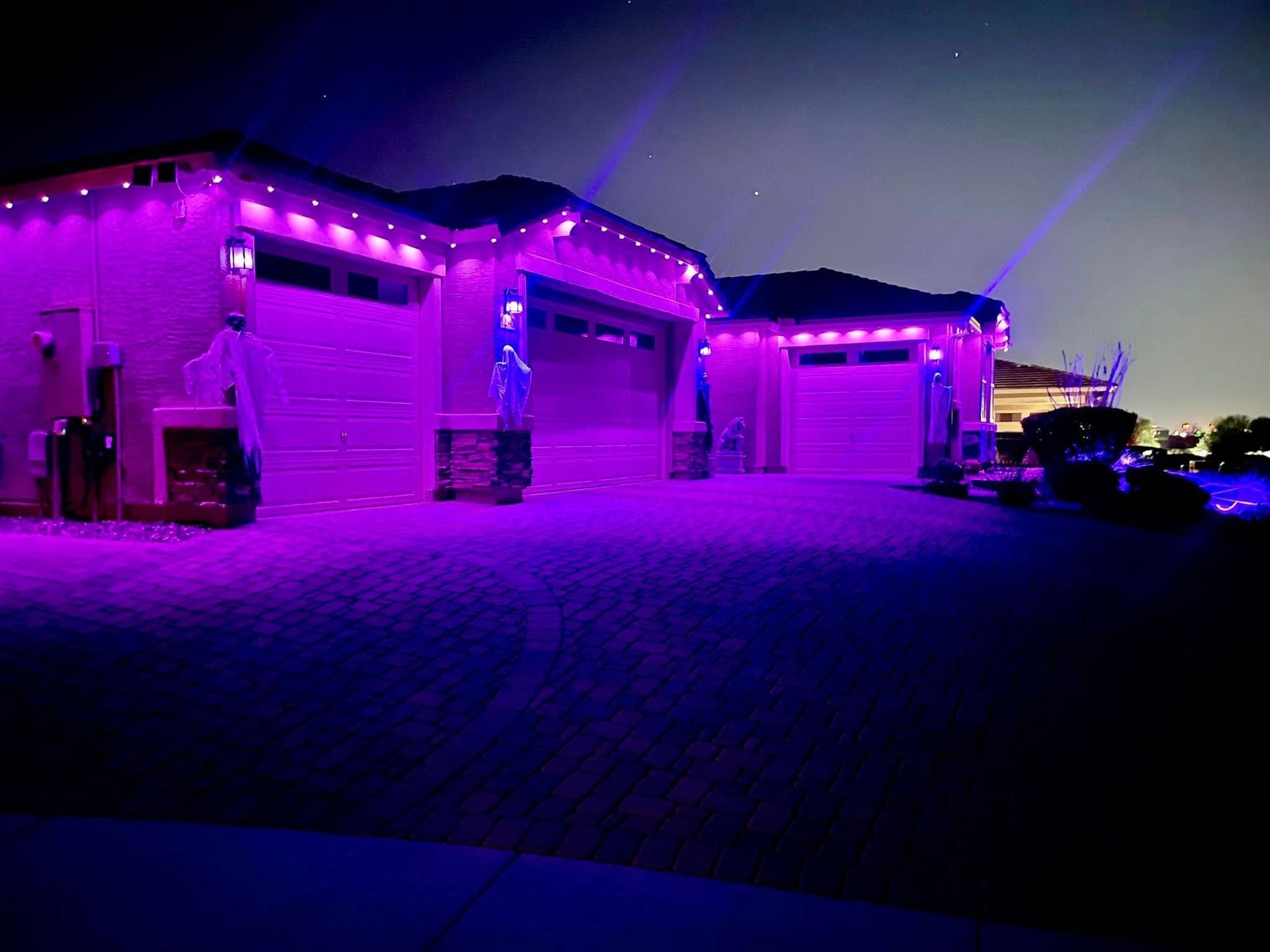 A house exterior illuminated by purple lights. Garage doors and roofline are outlined. Evening setting.