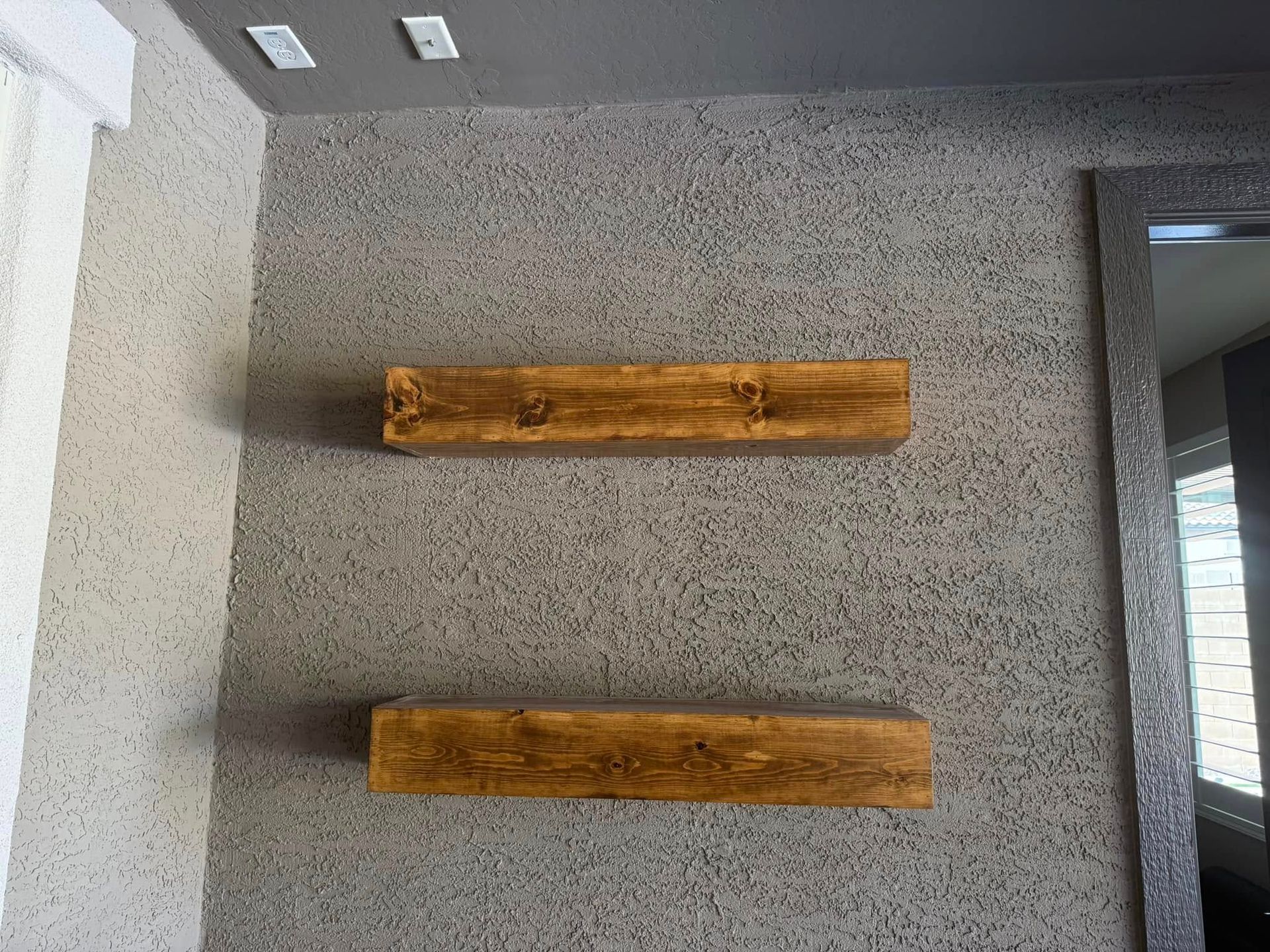 Two wooden shelves mounted on a textured gray wall, next to a silver-framed mirror.