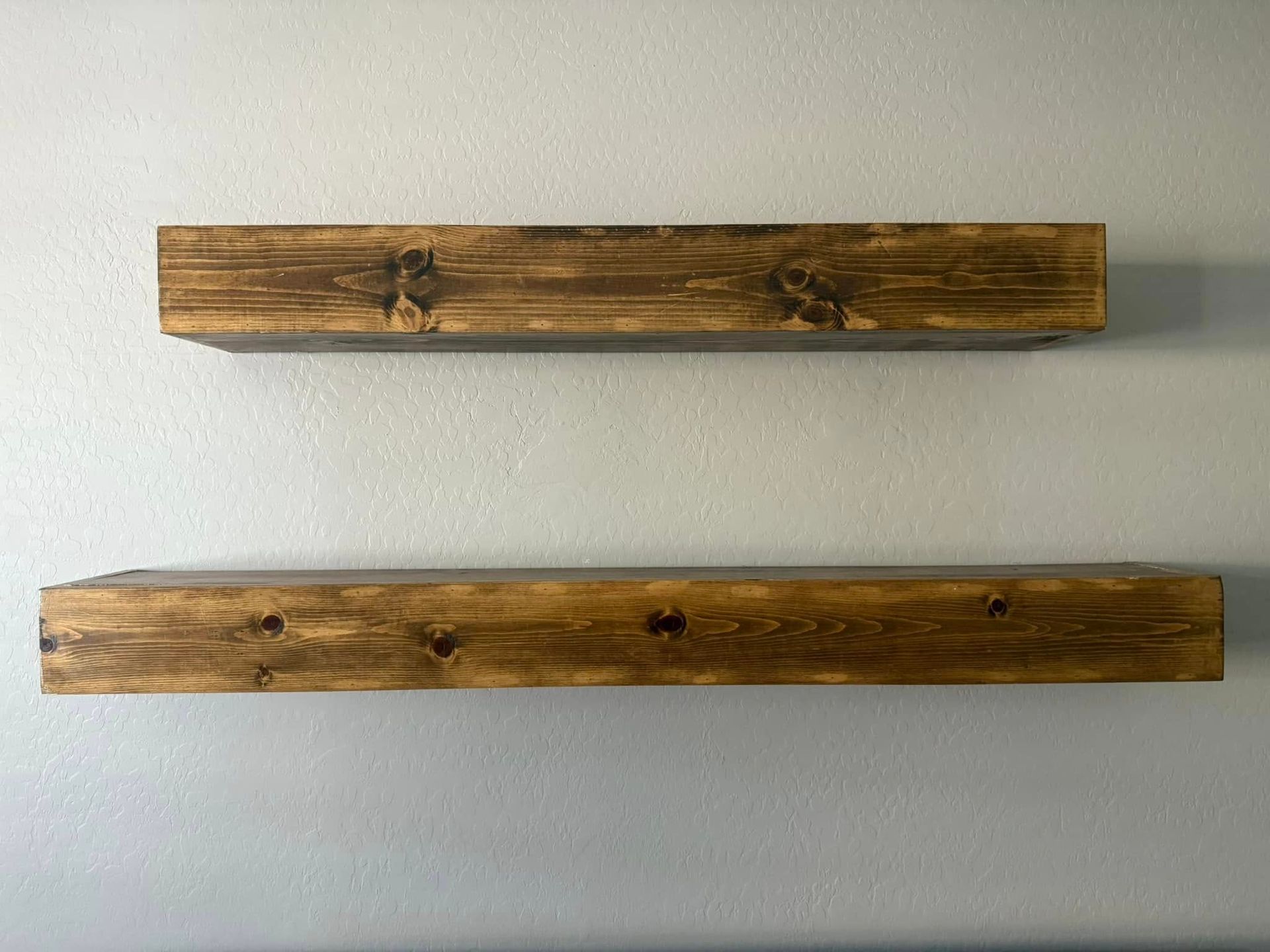 Two stained, wooden floating shelves mounted on a light gray wall.