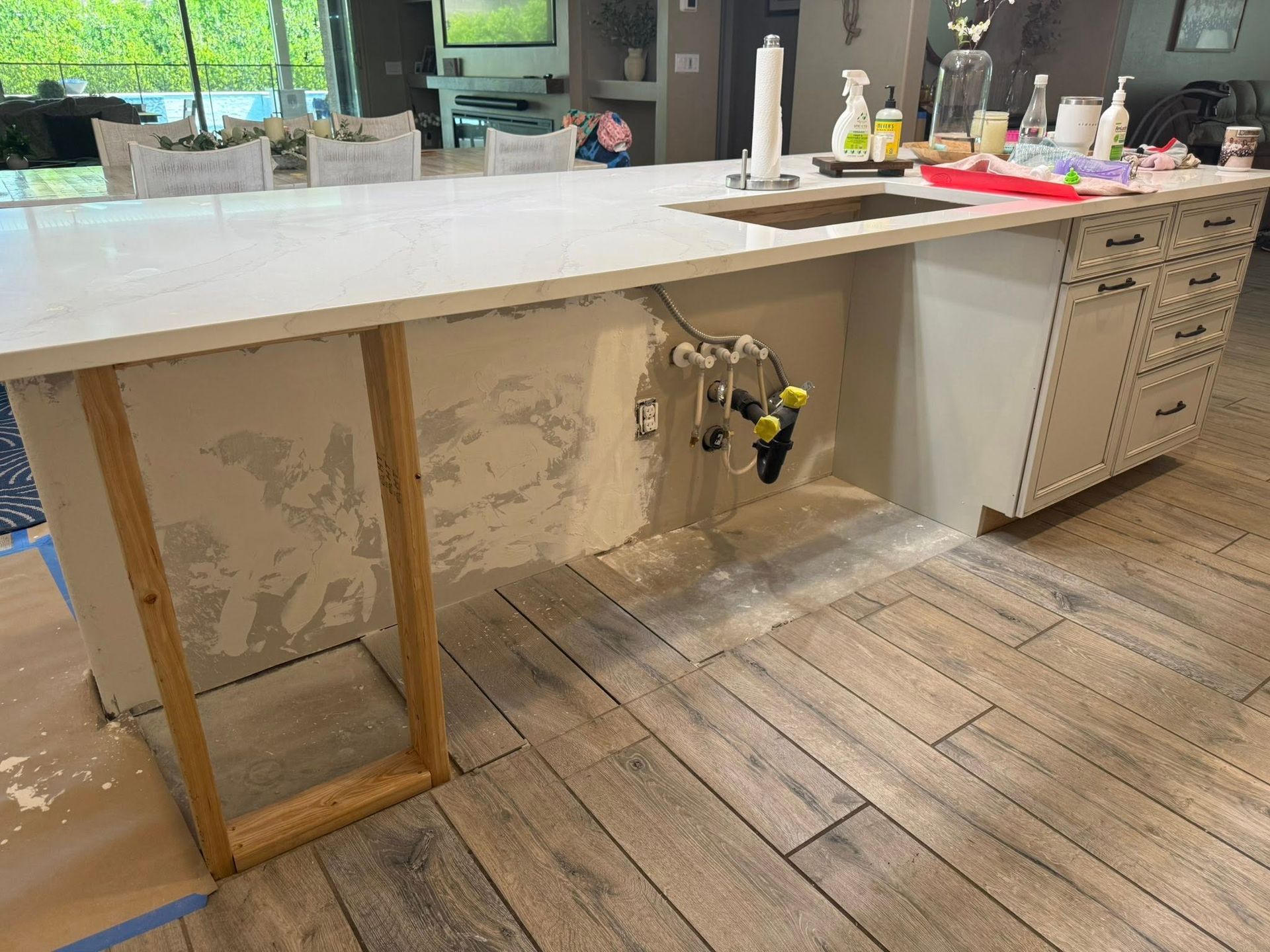 Kitchen island with exposed plumbing and unfinished drywall, supported by temporary wooden frame.