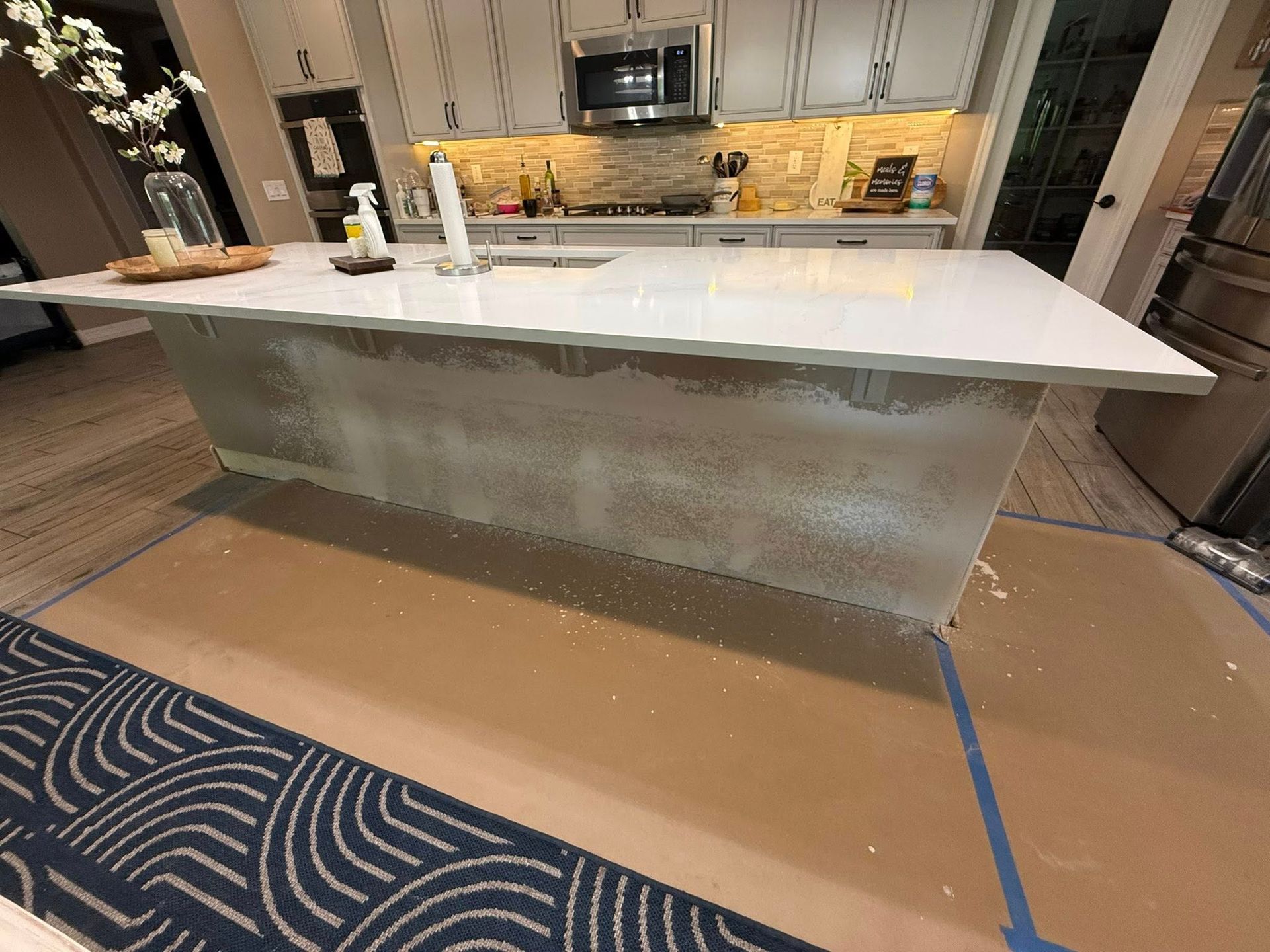 Kitchen island with white countertop. The island is being renovated, covered in drop cloths, and tools.