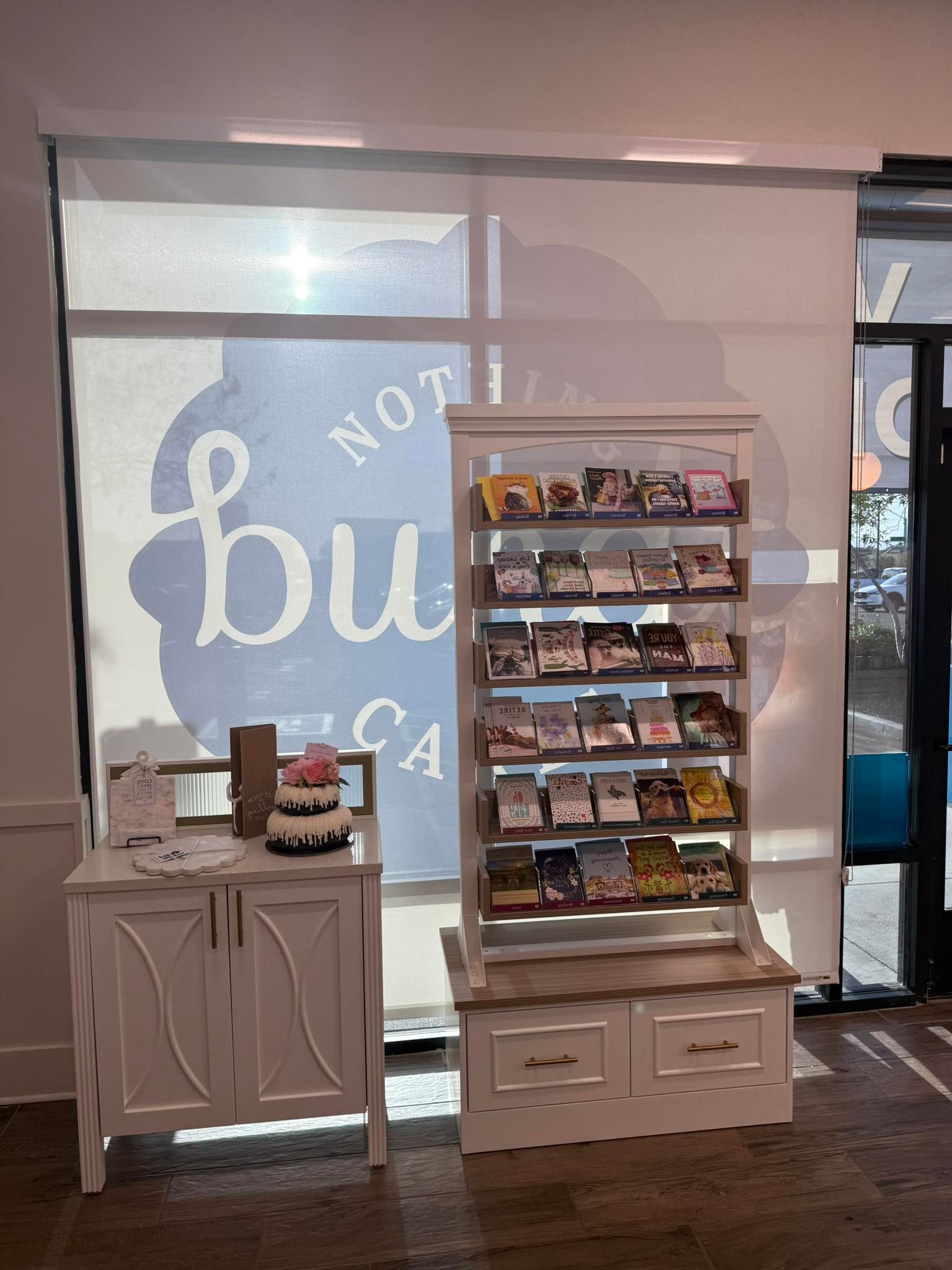 A white display case with various pamphlets, a cabinet with a cake, near a window with a logo.
