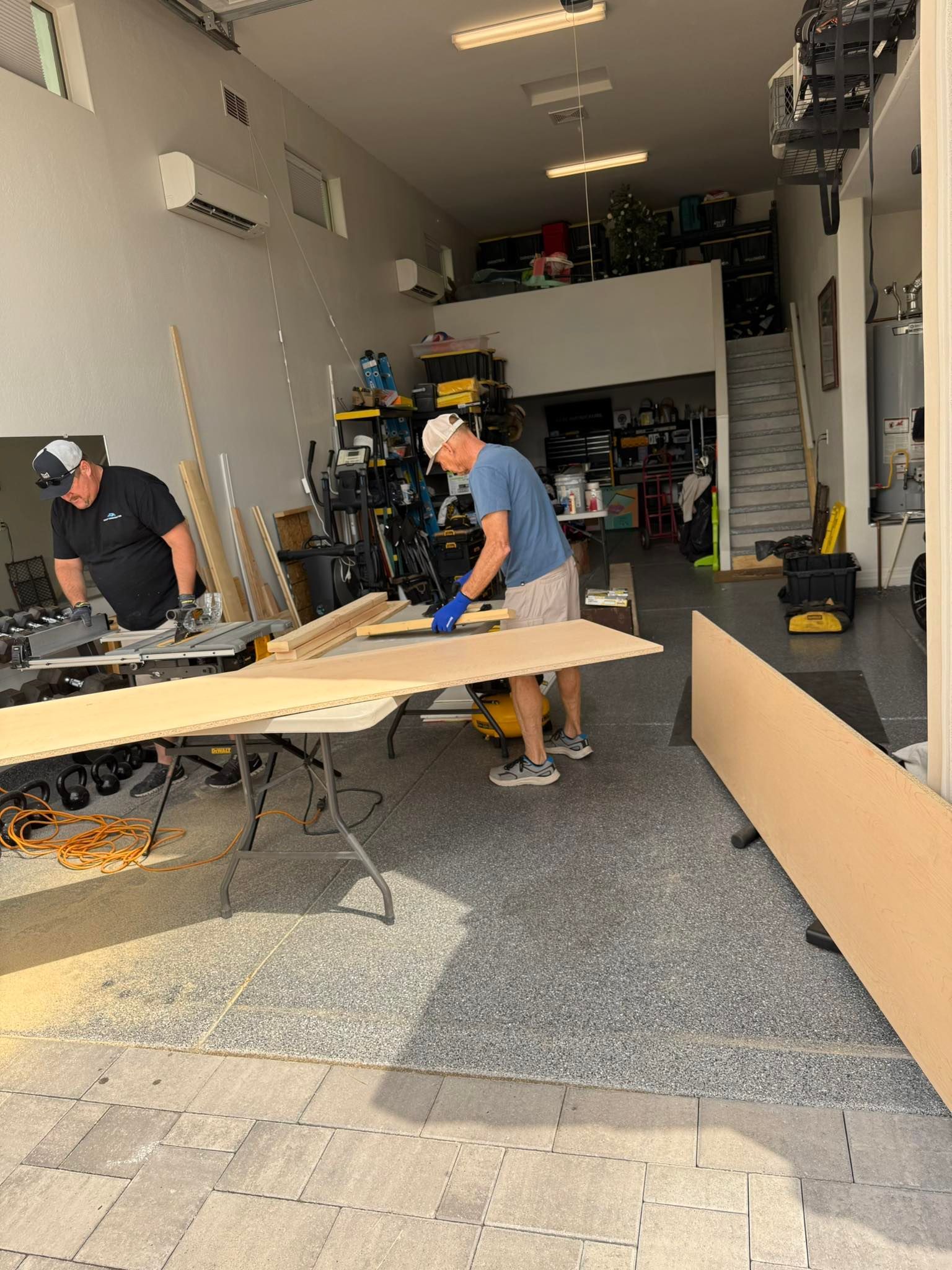Two men in a garage cutting wood with saws. Tools and supplies are in the background.
