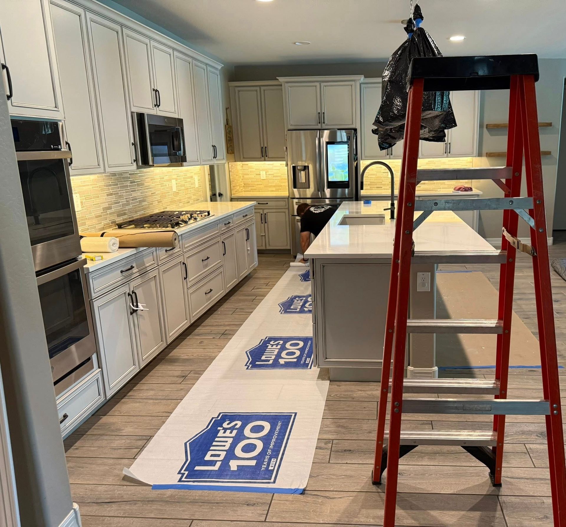 Kitchen remodel in progress with white cabinets, island, and red ladder.