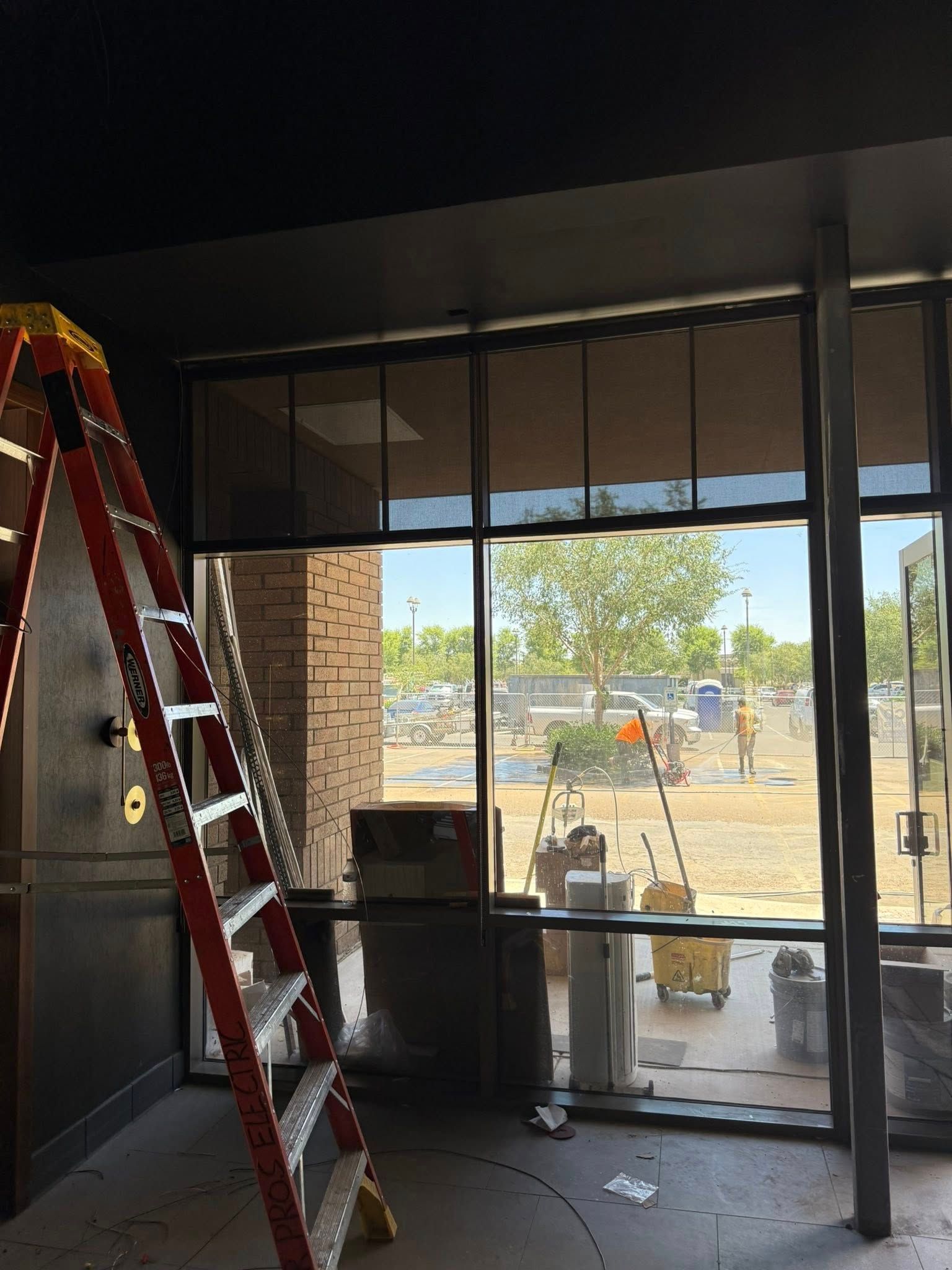 Red ladder leaning against a dark wall next to a large window overlooking a construction site.