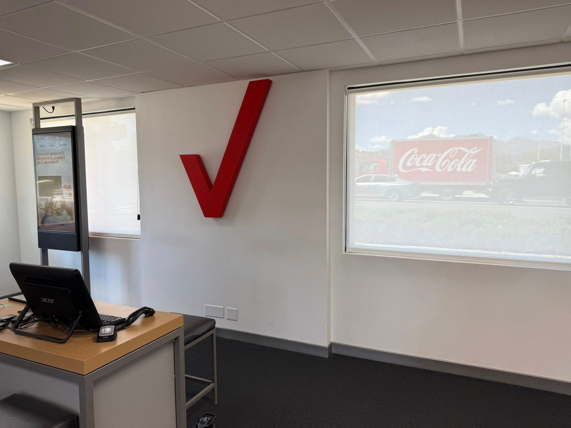 Verizon logo on a white office wall. A Coca-Cola sign is visible through the window.