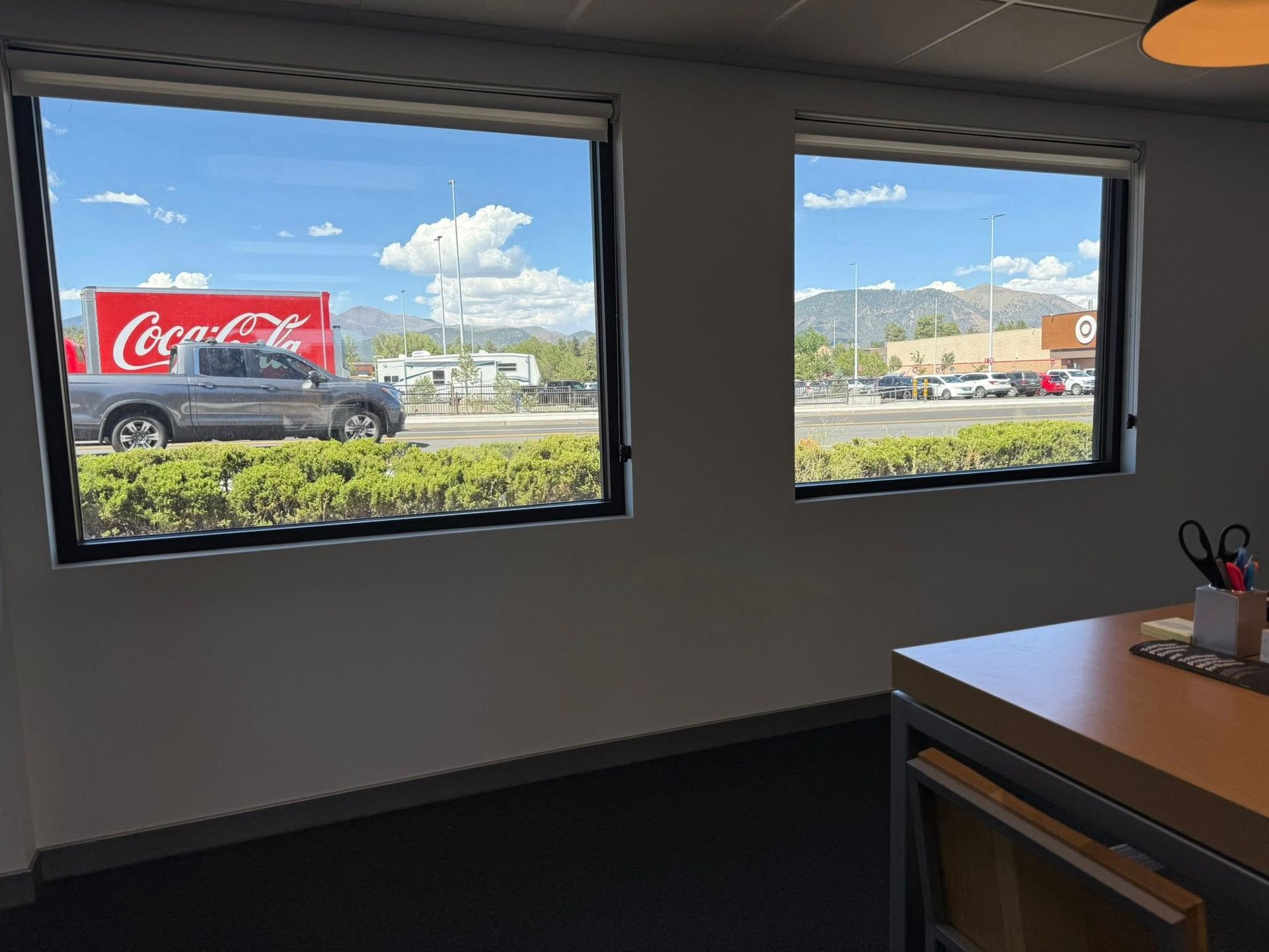 Two windows overlooking a street scene with a Coca-Cola truck and mountains on a sunny day.