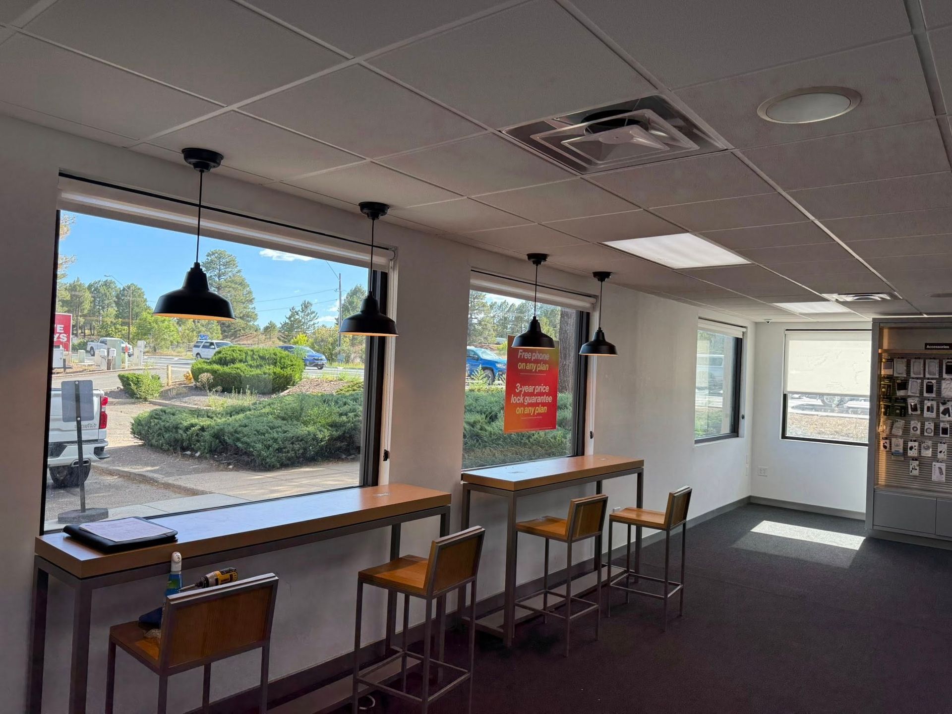 Interior of a cafe with bar seating, large windows overlooking outdoor landscaping, and pendant lights.