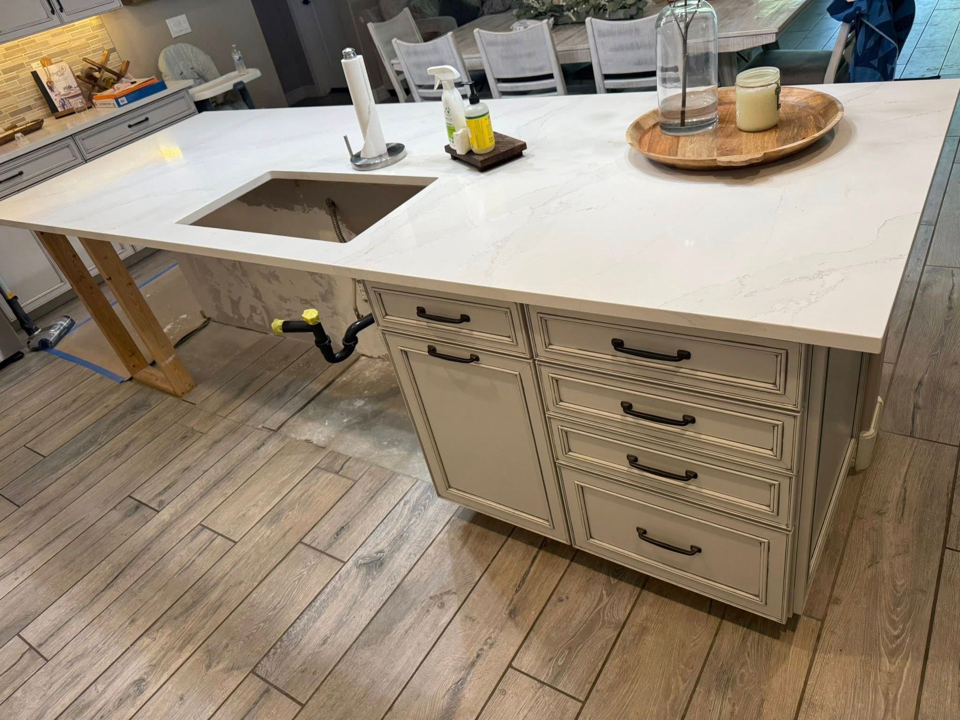 Kitchen island with white countertop, sink, and cabinets. Wooden flooring and light beige cabinets.