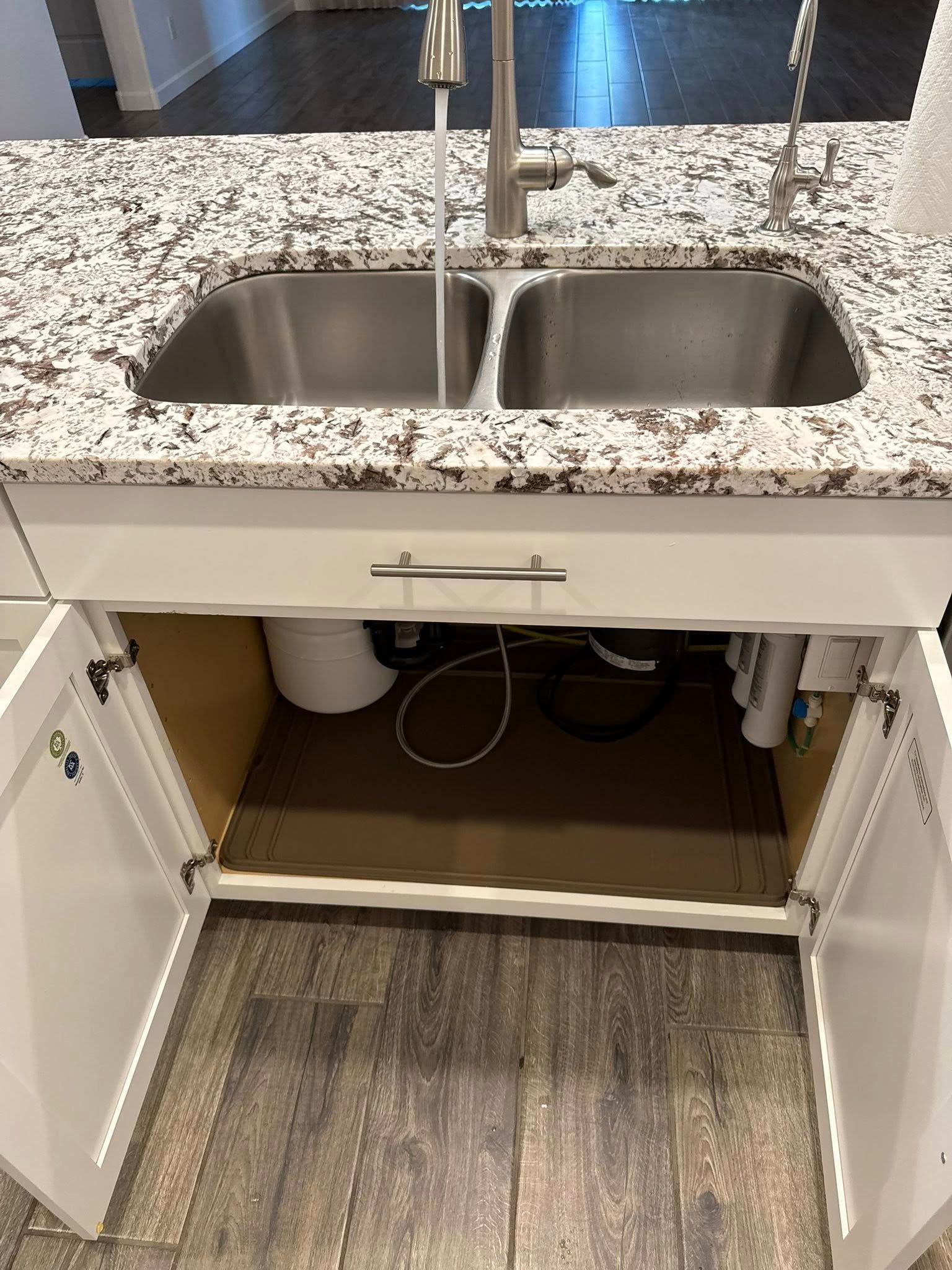Kitchen sink with open cabinet doors. Underside shows plumbing, filters, and a water filter tank.