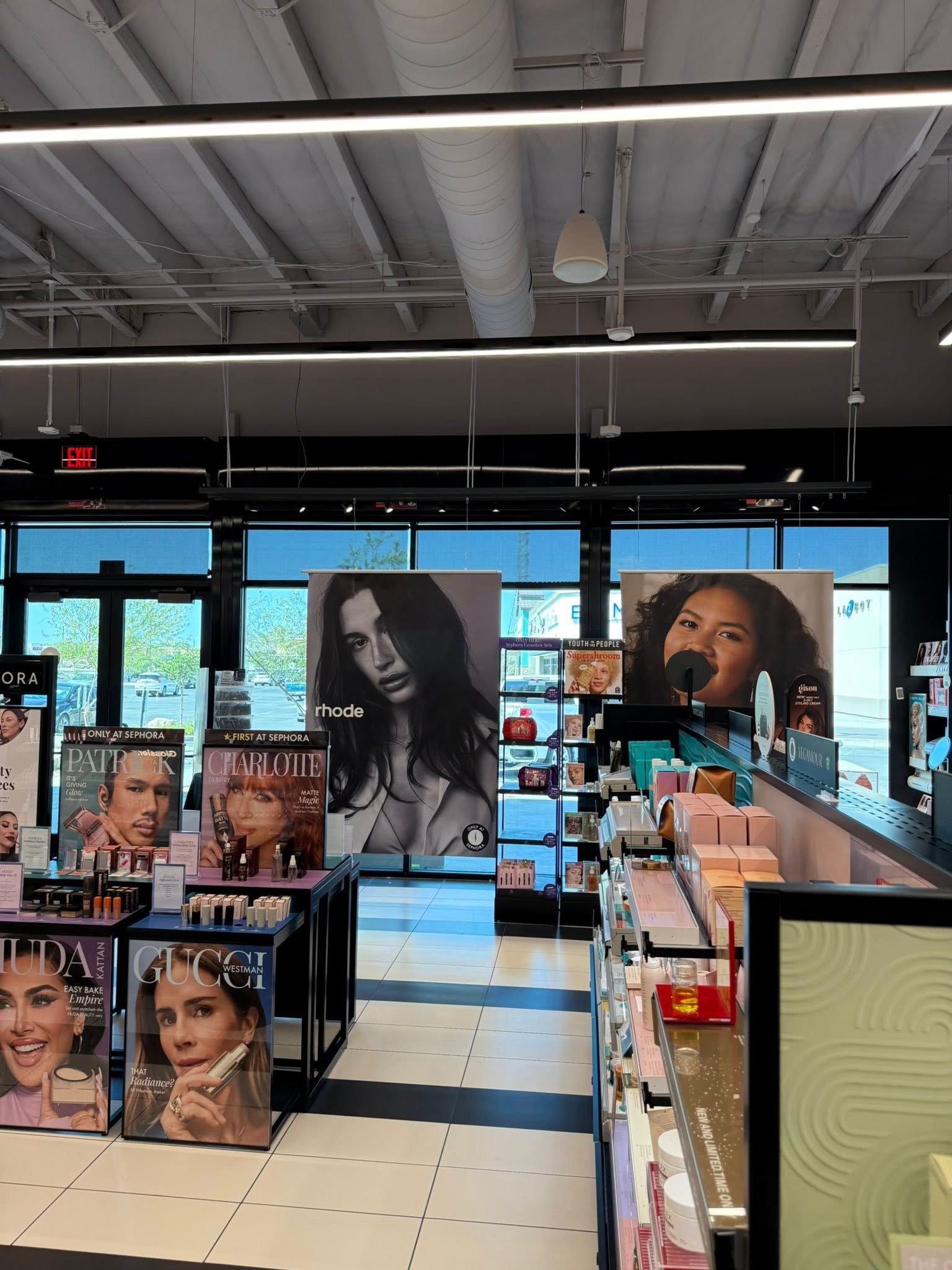 Interior of a makeup store with product displays, promotional posters, and large portraits hanging overhead.