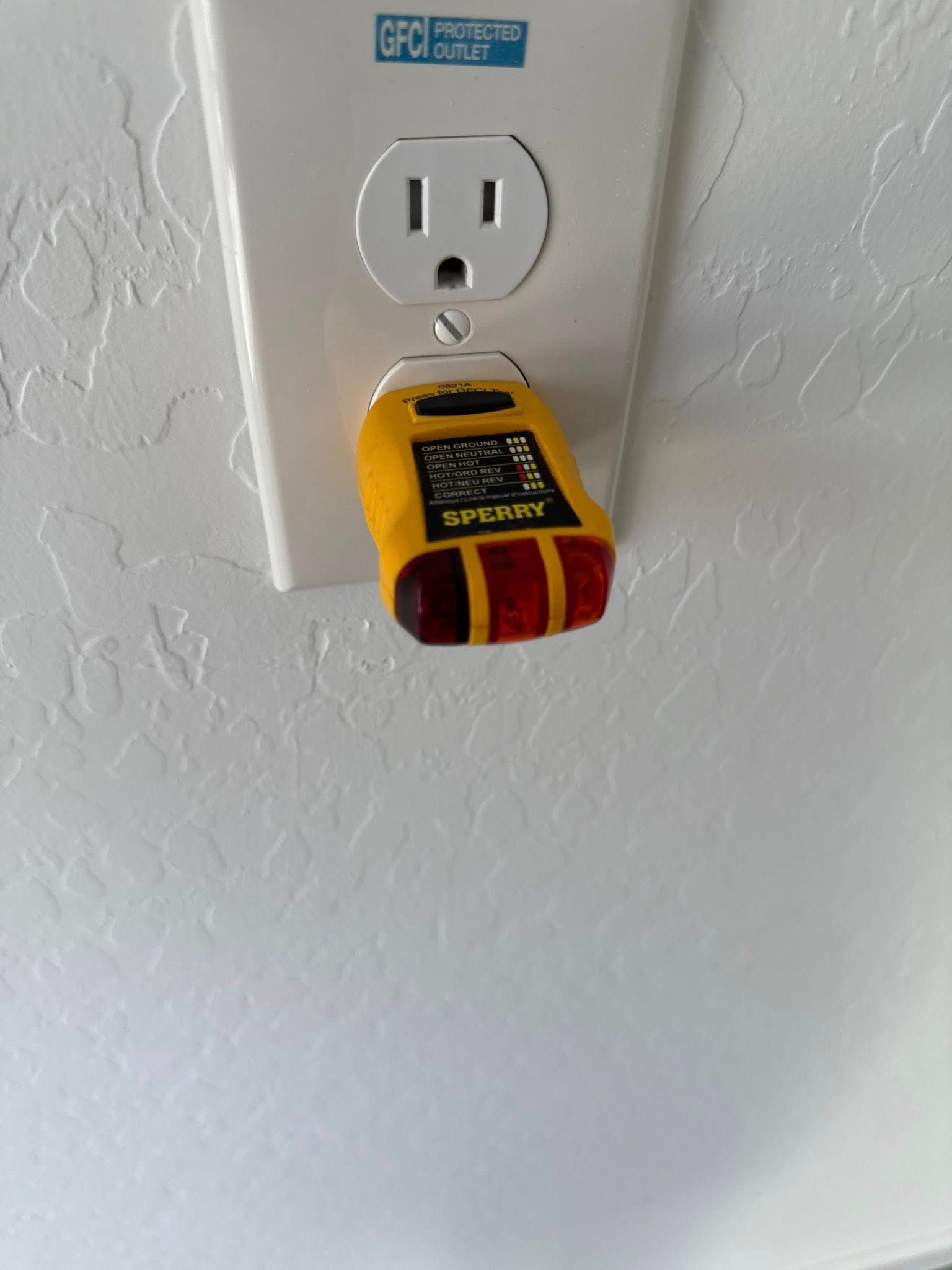 Yellow electrical outlet tester plugged into a white wall outlet.