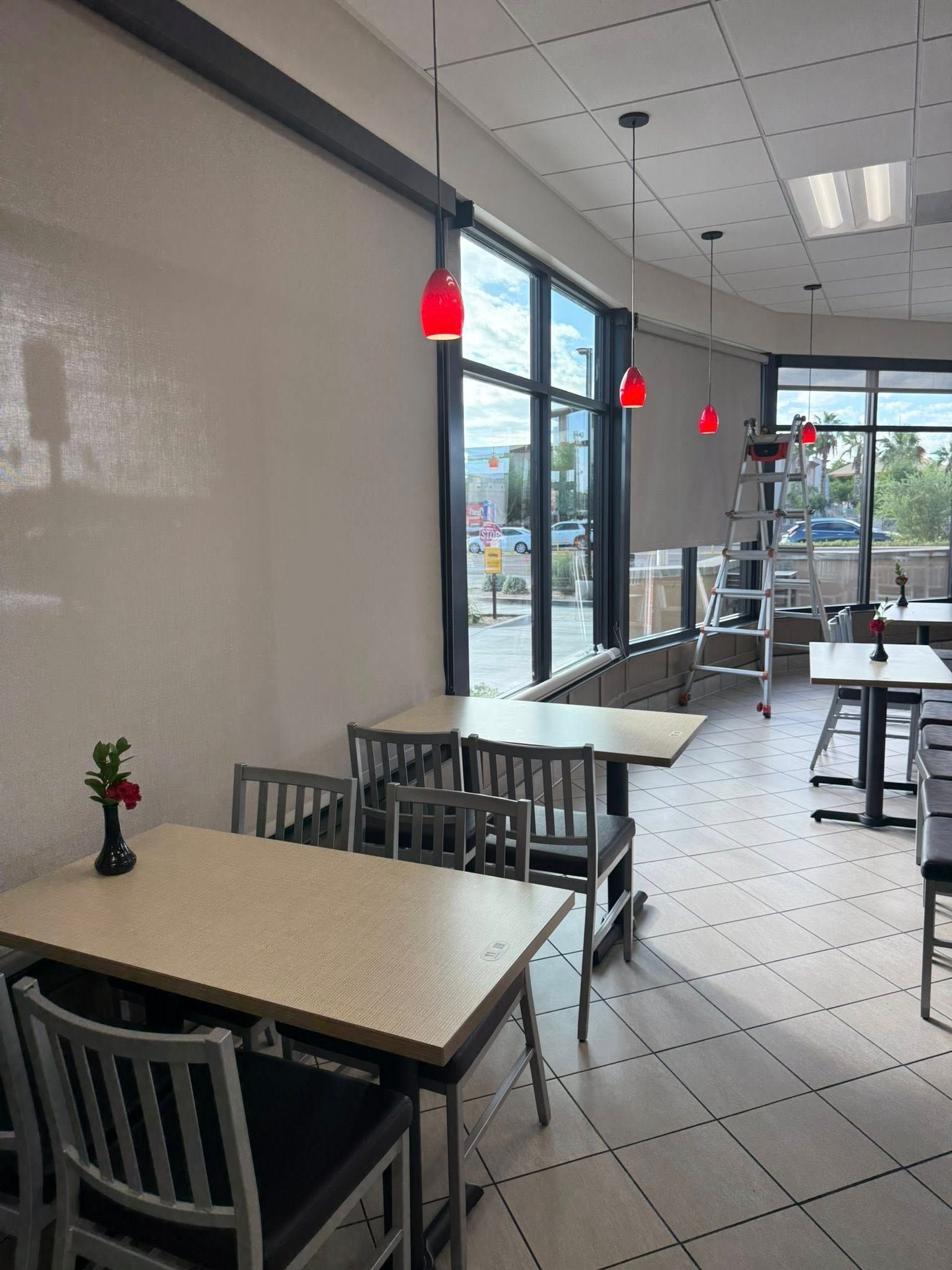 Restaurant interior with tables, chairs, red pendant lights, and a window overlooking a street.