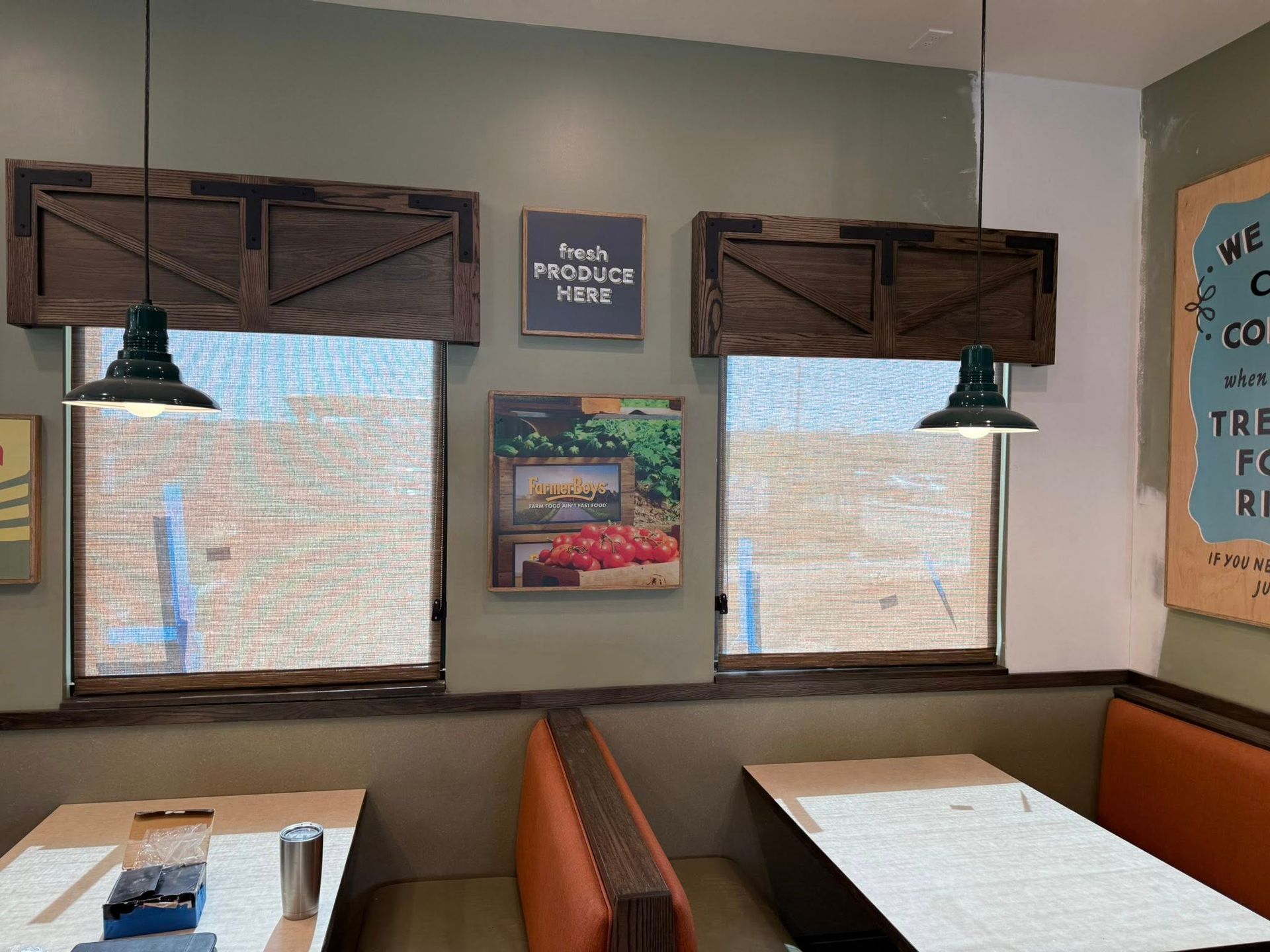 Restaurant booth seating with windows, brown wooden shades, green pendant lights, and wall art.