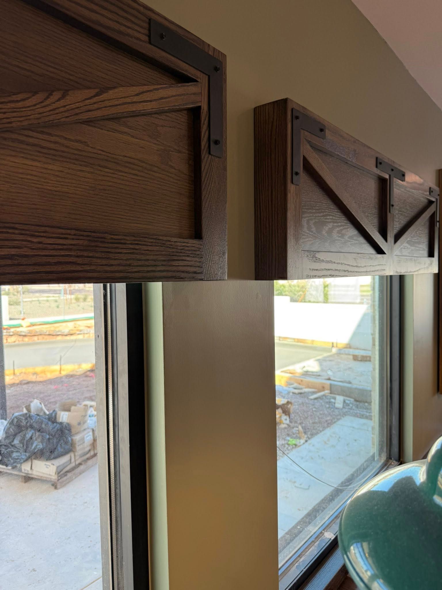 Wooden window valance with black metal accents and visible window frame and view.