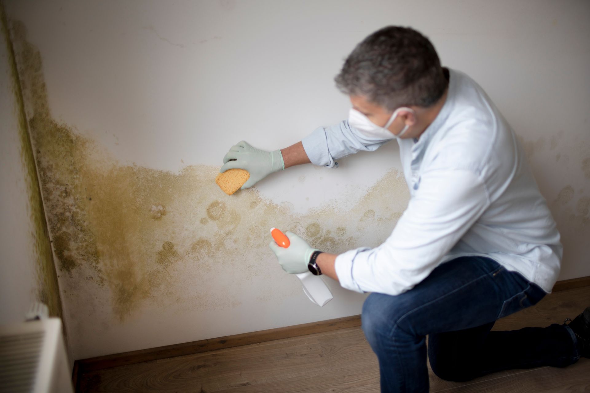 A man wearing a mask and gloves is cleaning a wall with a sponge.