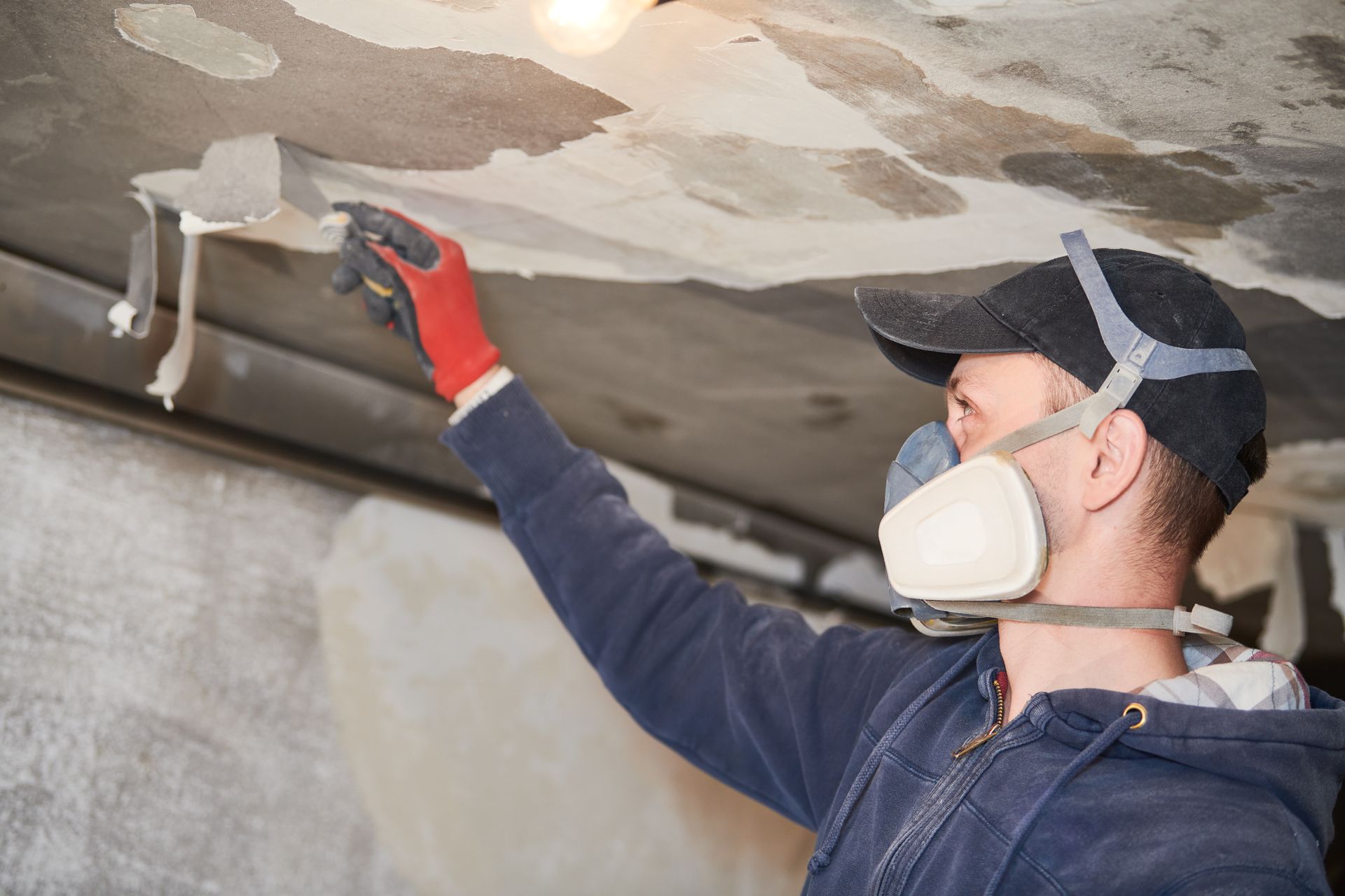 A man wearing a mask and gloves is working on a ceiling.