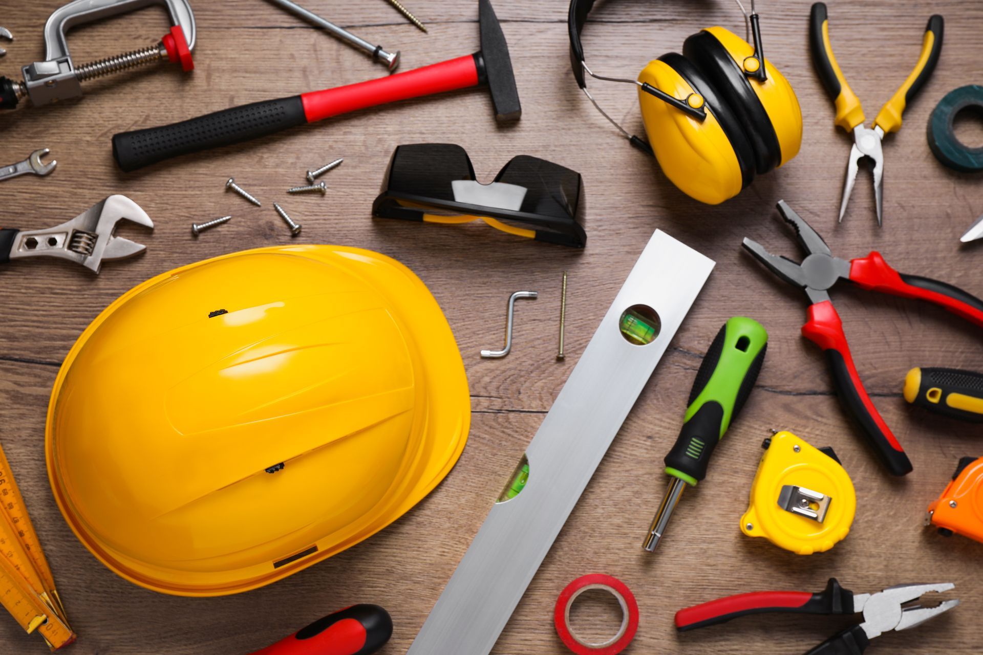 A hard hat is surrounded by a variety of construction tools on a wooden table.