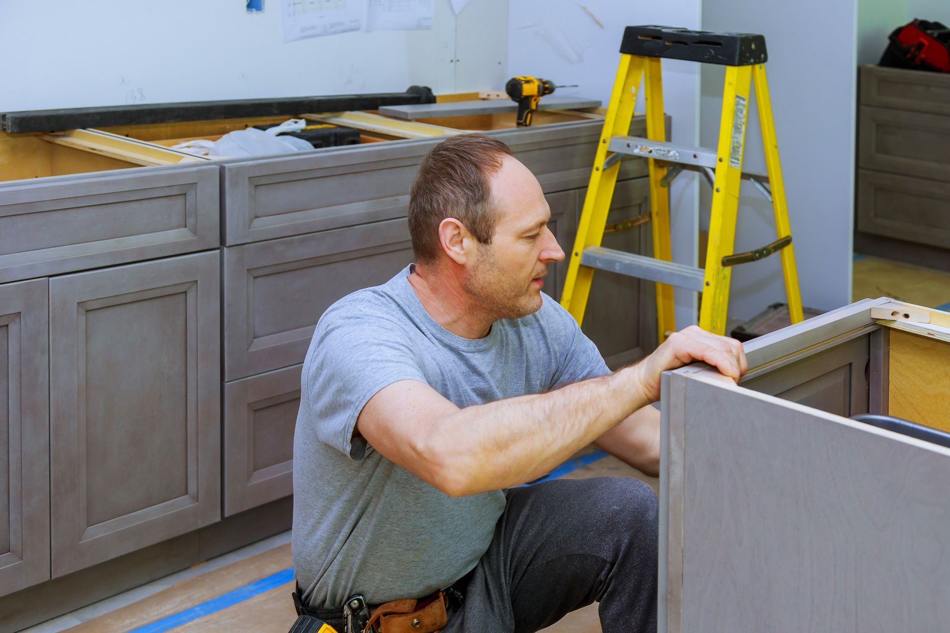 A man is kneeling down in a kitchen working on a cabinet.