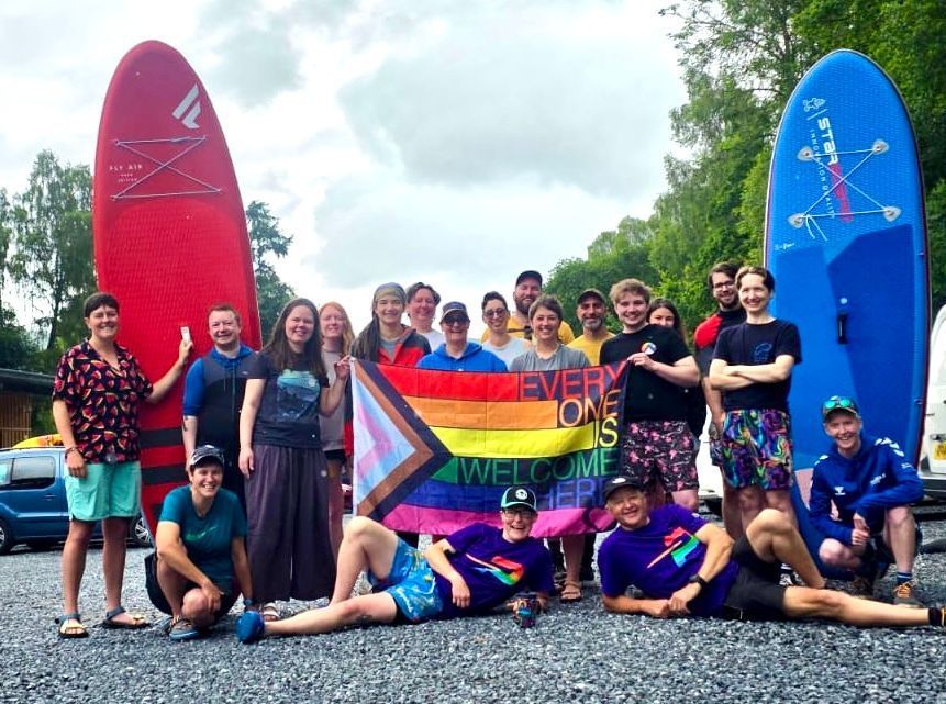 A group of people are posing for a picture while holding a rainbow flag.