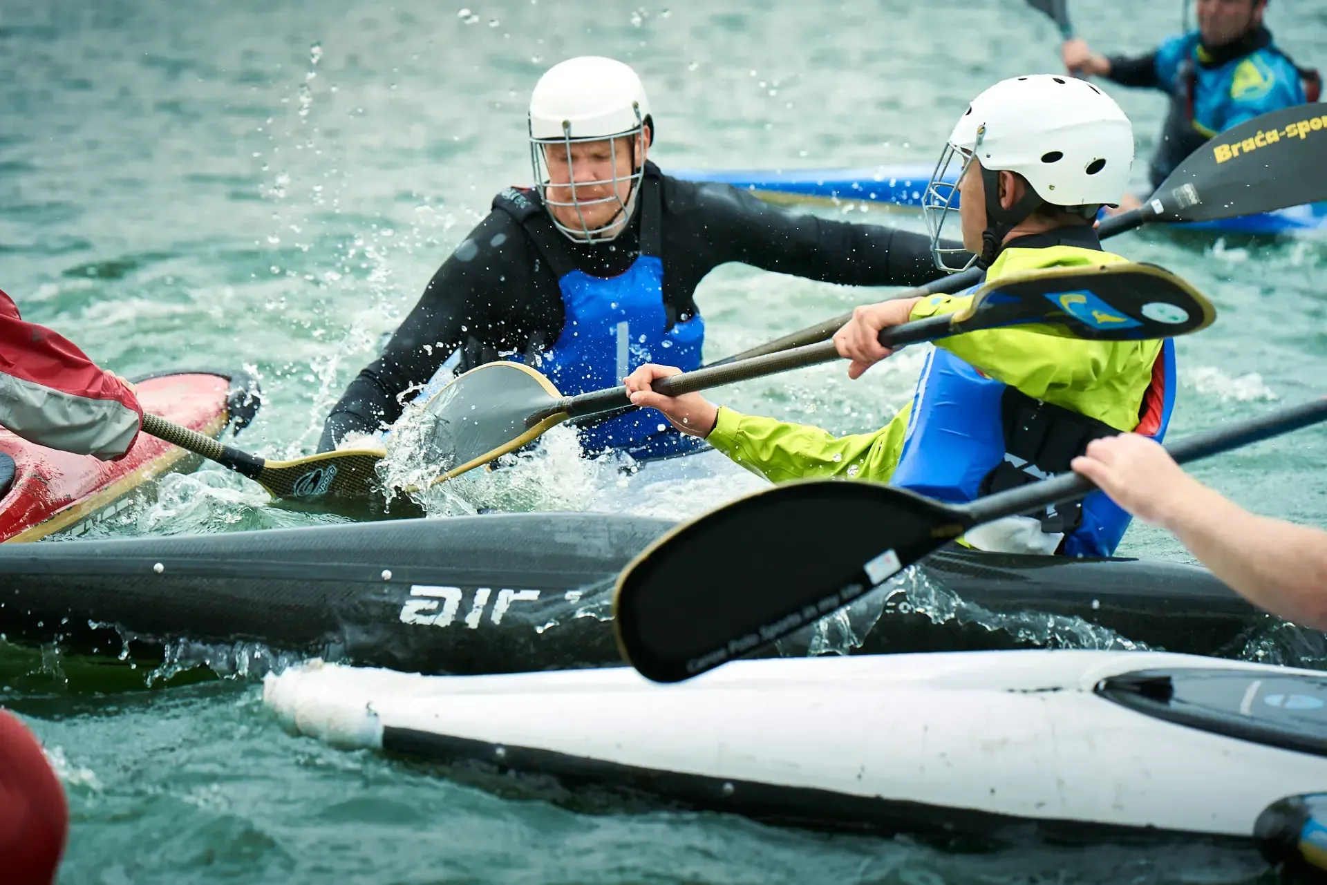 Kayakers colliding in water during a competition, splashing water. Men wearing helmets and paddling gear.