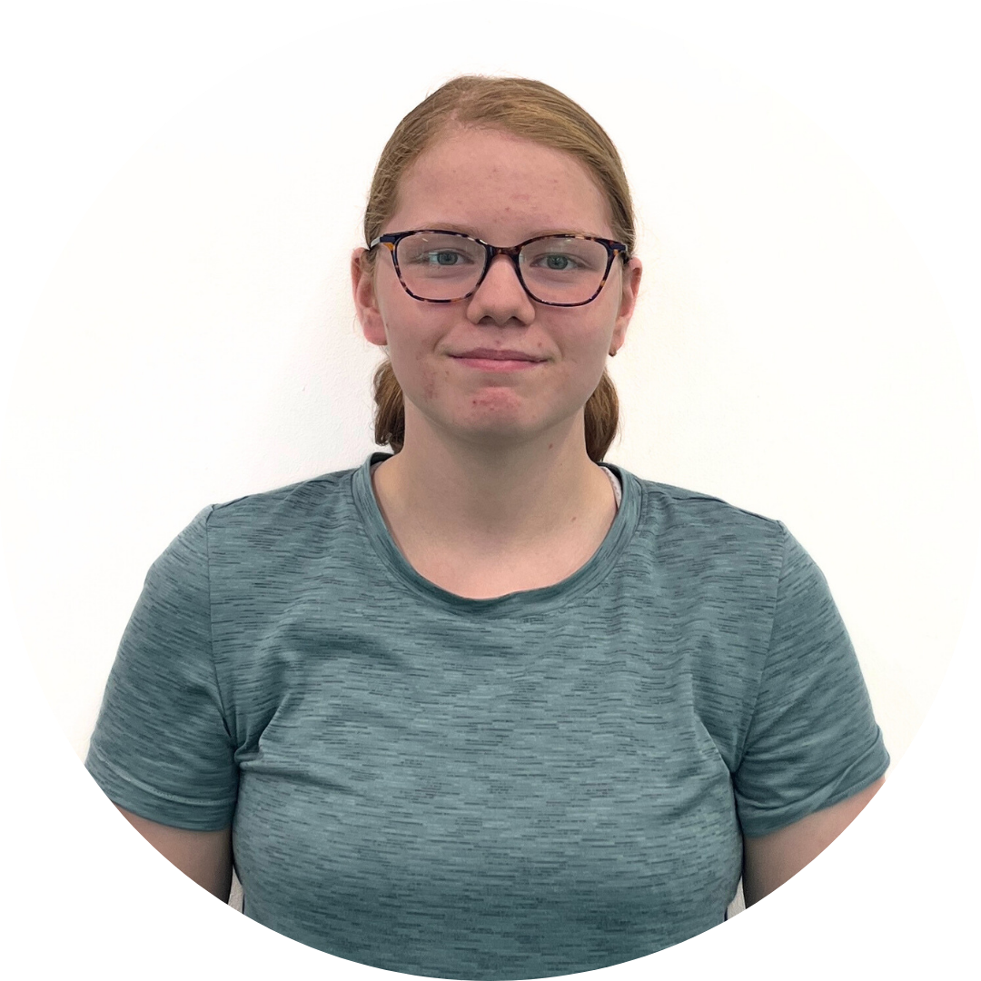 A young woman with light skin, glasses, and red hair smiles. She wears a teal shirt in front of a white background.