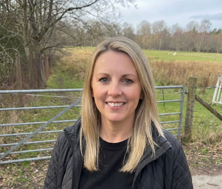 A man with a beard and glasses smiles, holding a small, fluffy dog outdoors under a cloudy sky.