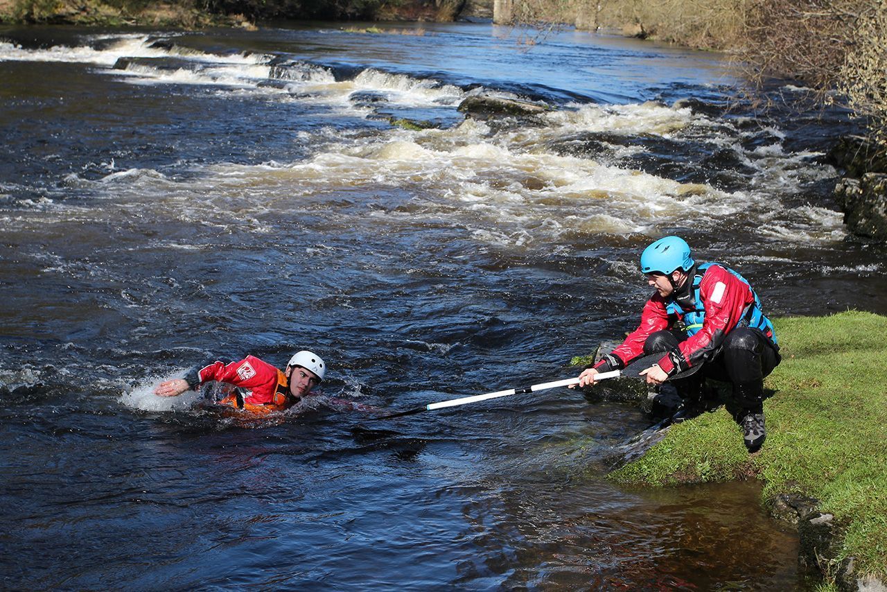 A man is helping another man out of a river.